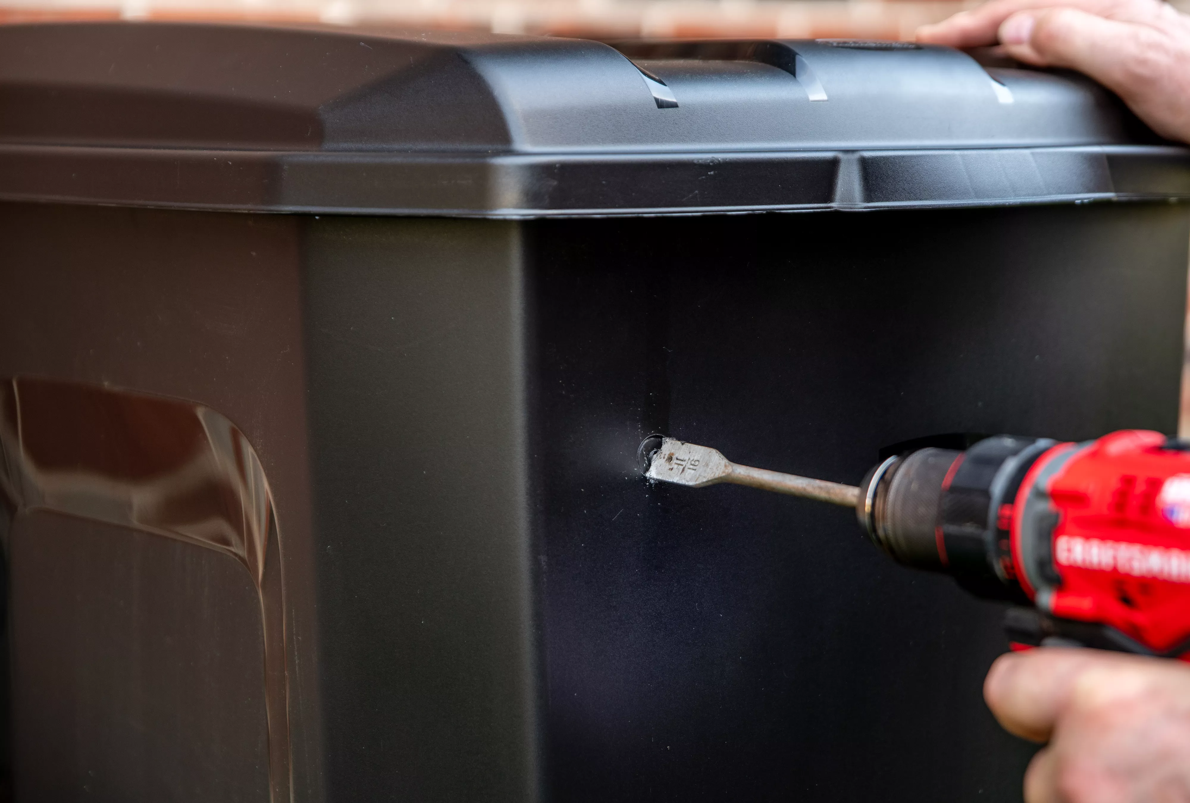 drilling a hole into the side of the bin, starting a few inches from the lid