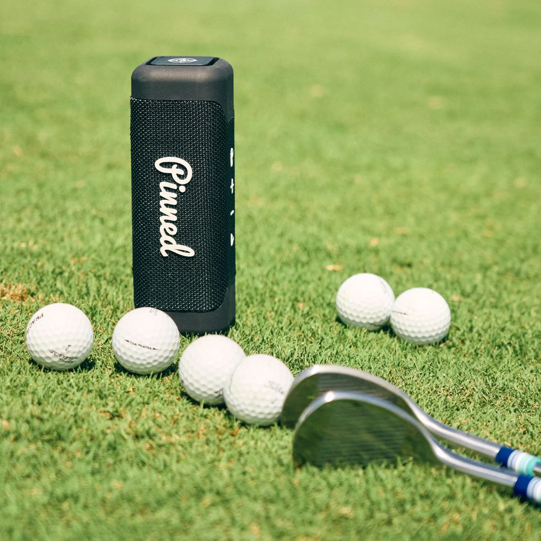 navy pinned golf speaker in grass with golf balls and golf clubs navy pinned golf speaker in grass with golf balls and golf clubs