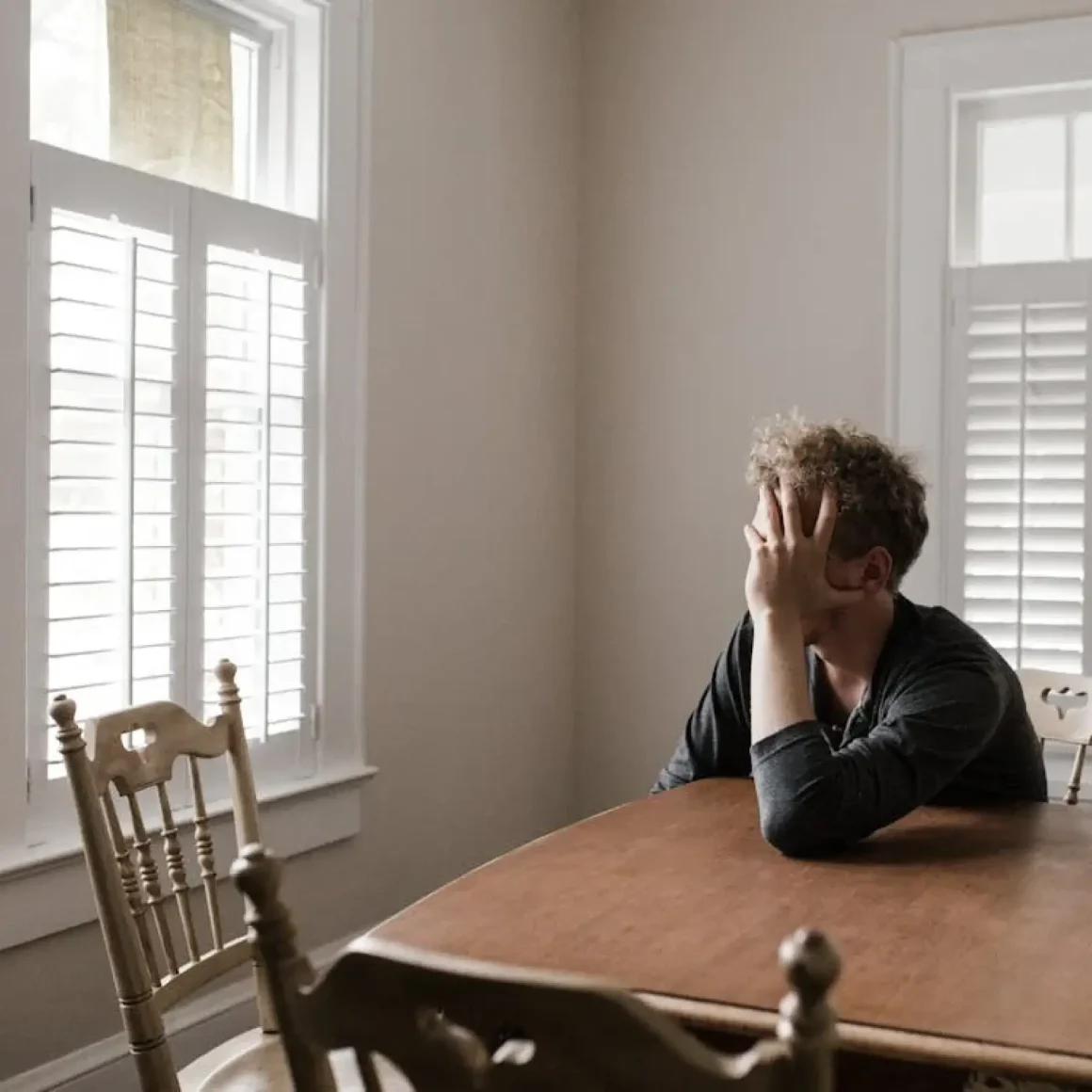 Man sitting at the dining room table, holding his head in his hand Man sitting at the dining room table, holding his head in his hand