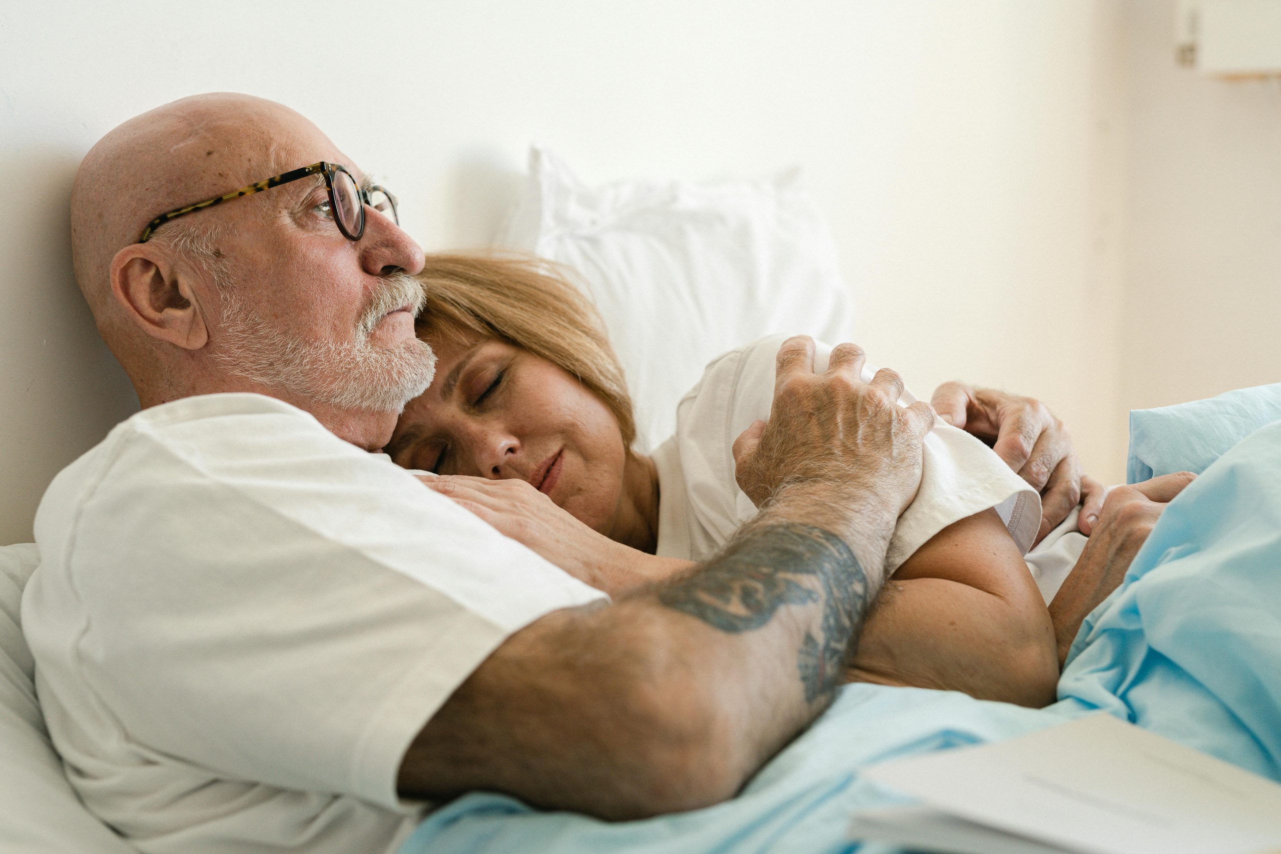 Man looking pensive in bed, as he holds his wife close Man looking pensive in bed, as he holds his wife close