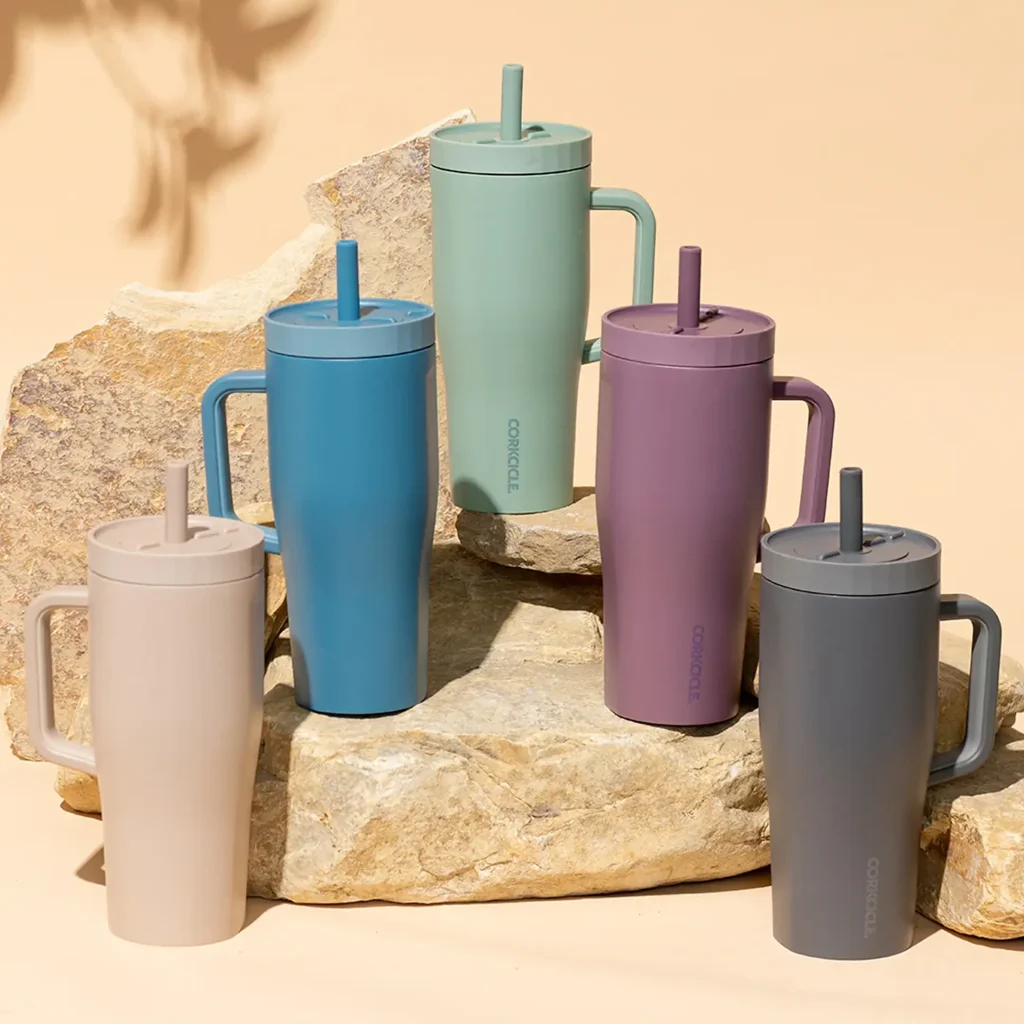 5 corkcicle water bottles placed on stones with a beige background