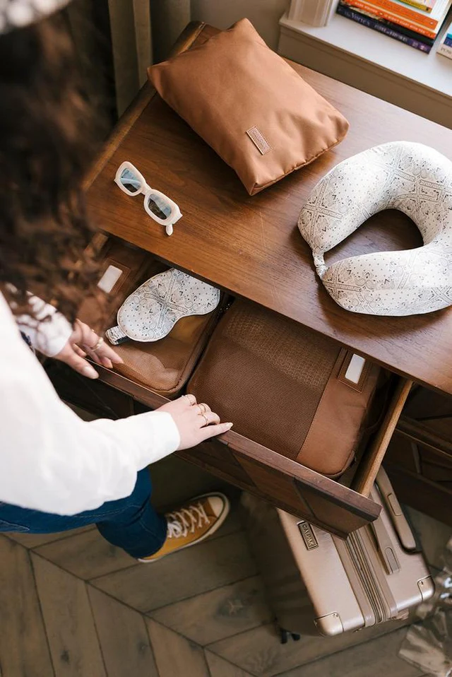 Woman opening hotel room drawer to retrieve one of two CALPAK Packing Cubes in color Hazel