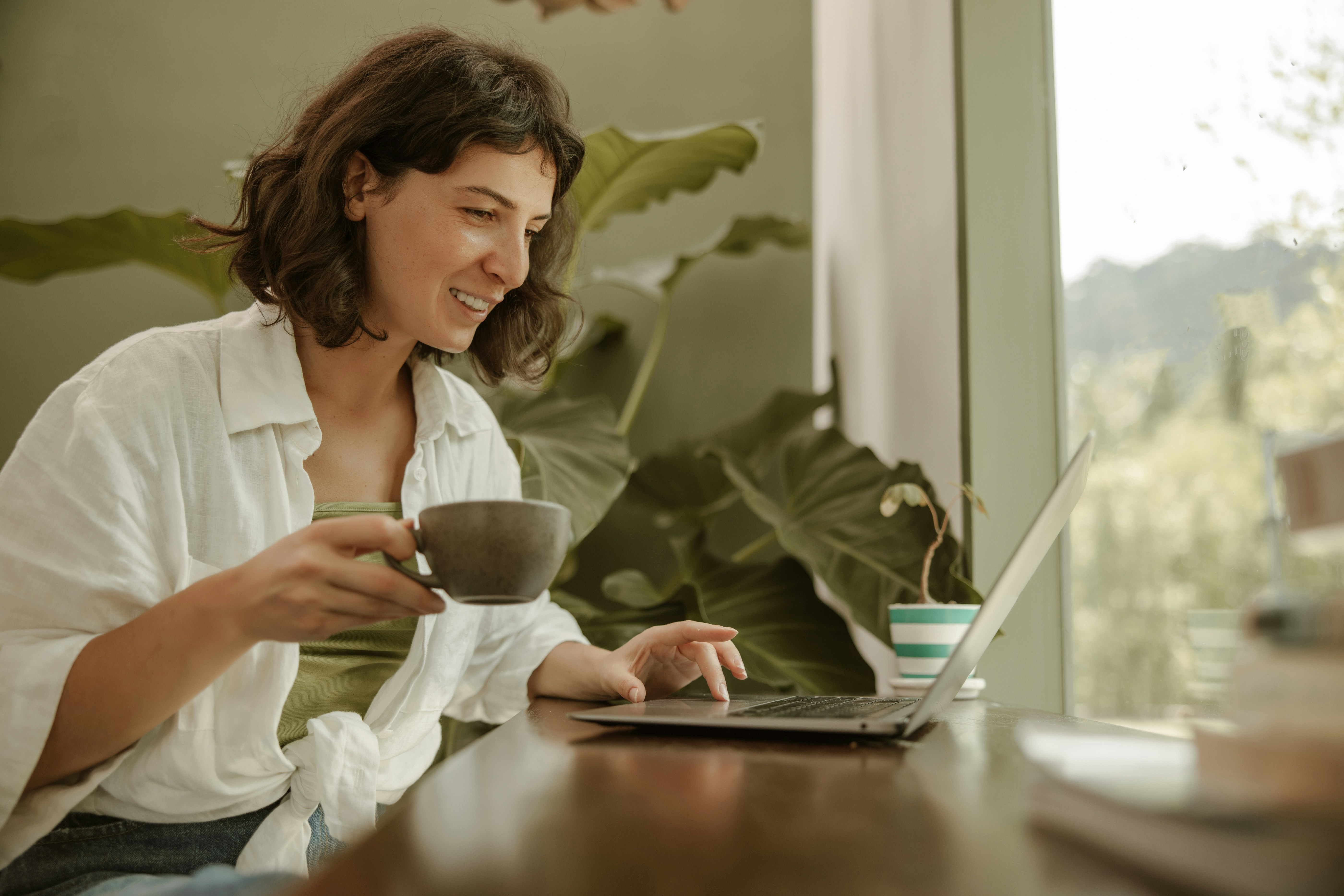 Woman smiling while using a laptop and holding a cup