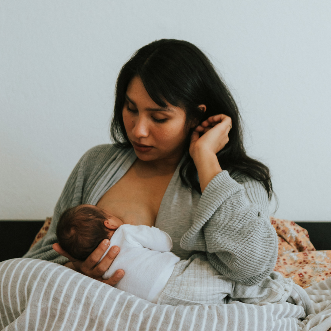 Mother breastfeeding her baby while sitting on a bed