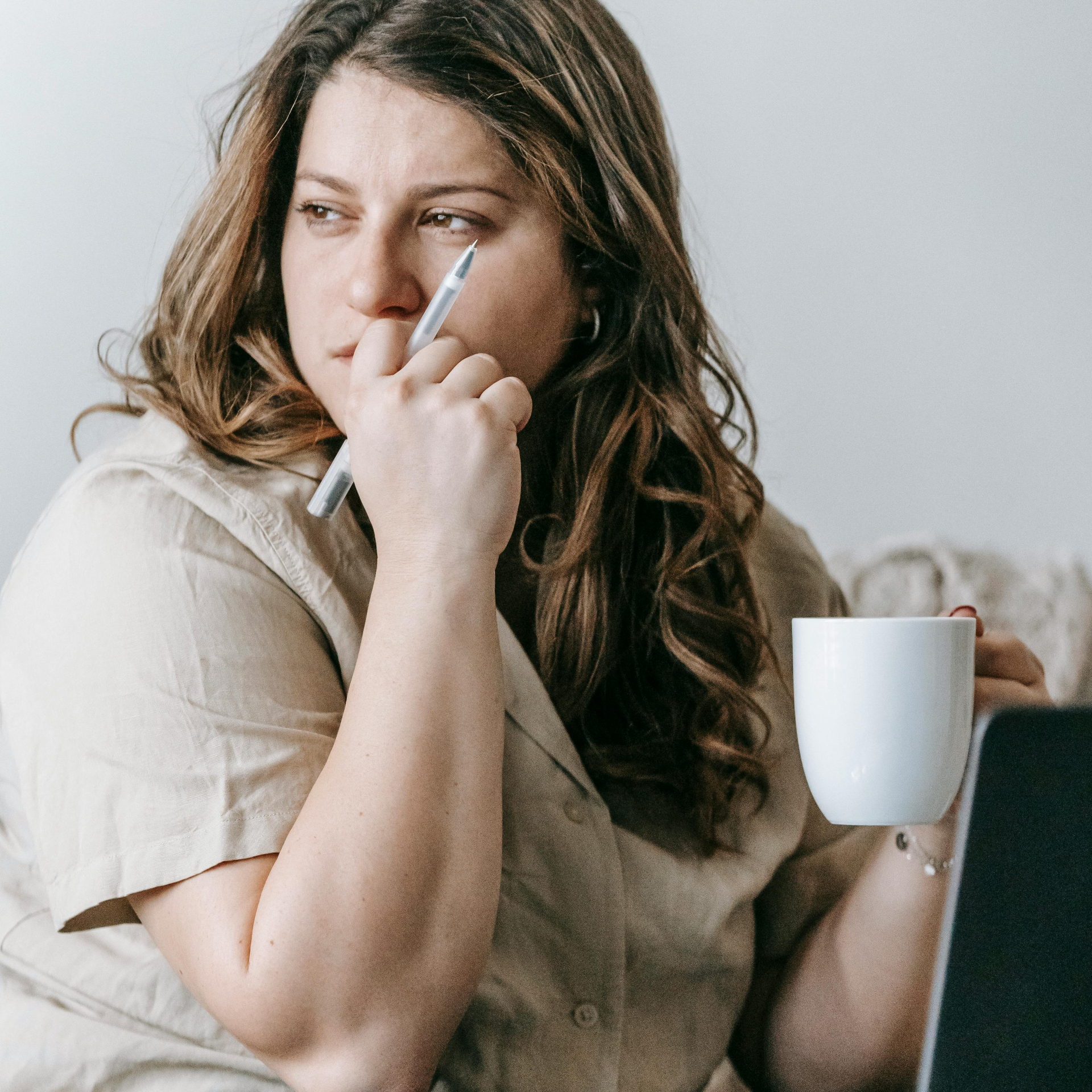 A contemplative GLP-1 patient sits thoughtfully with a pen in one hand and a coffee mug in the other