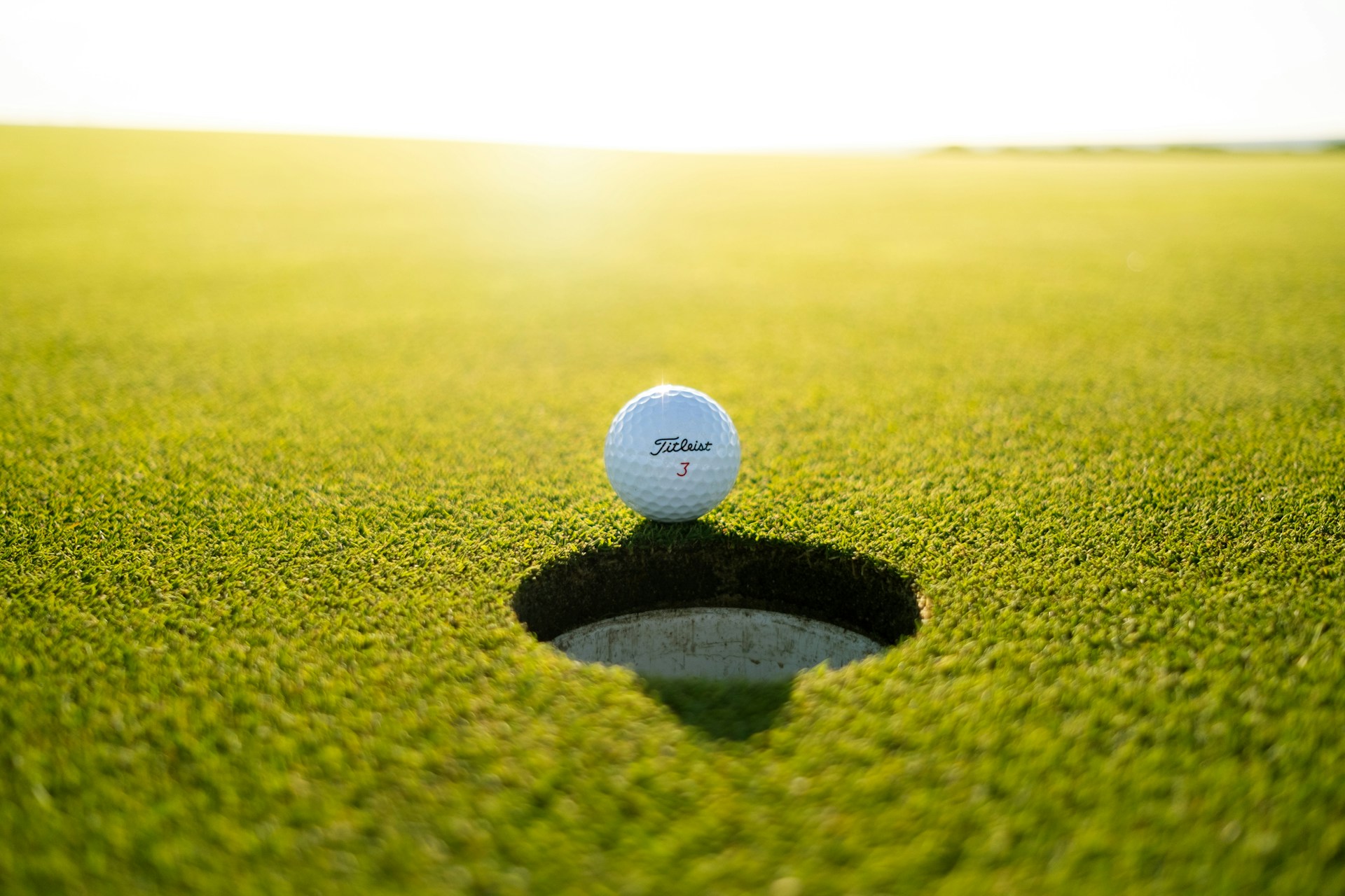 Golf ball resting on the edge of a hole on a golf course
