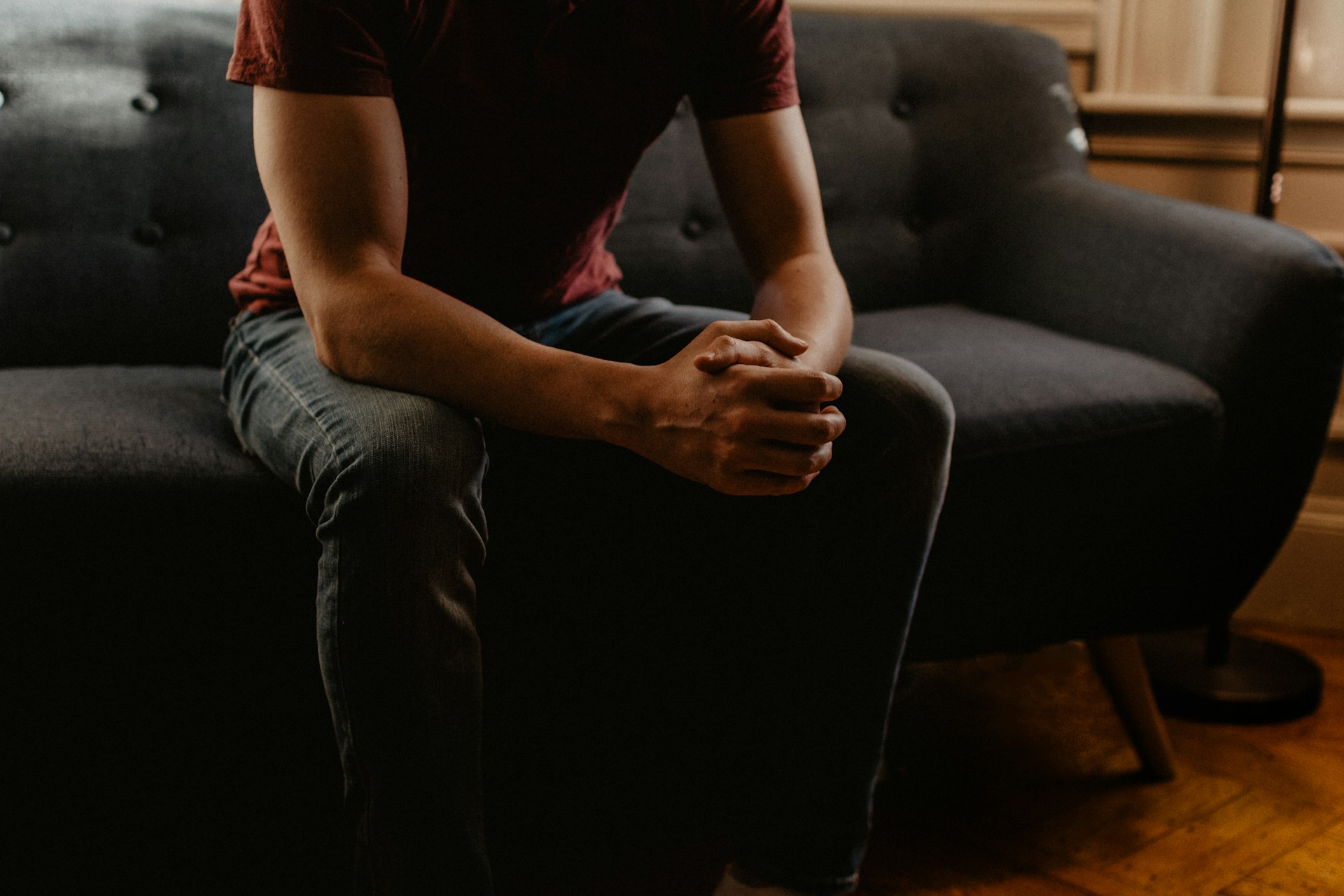 Person sitting on a couch with hands clasped