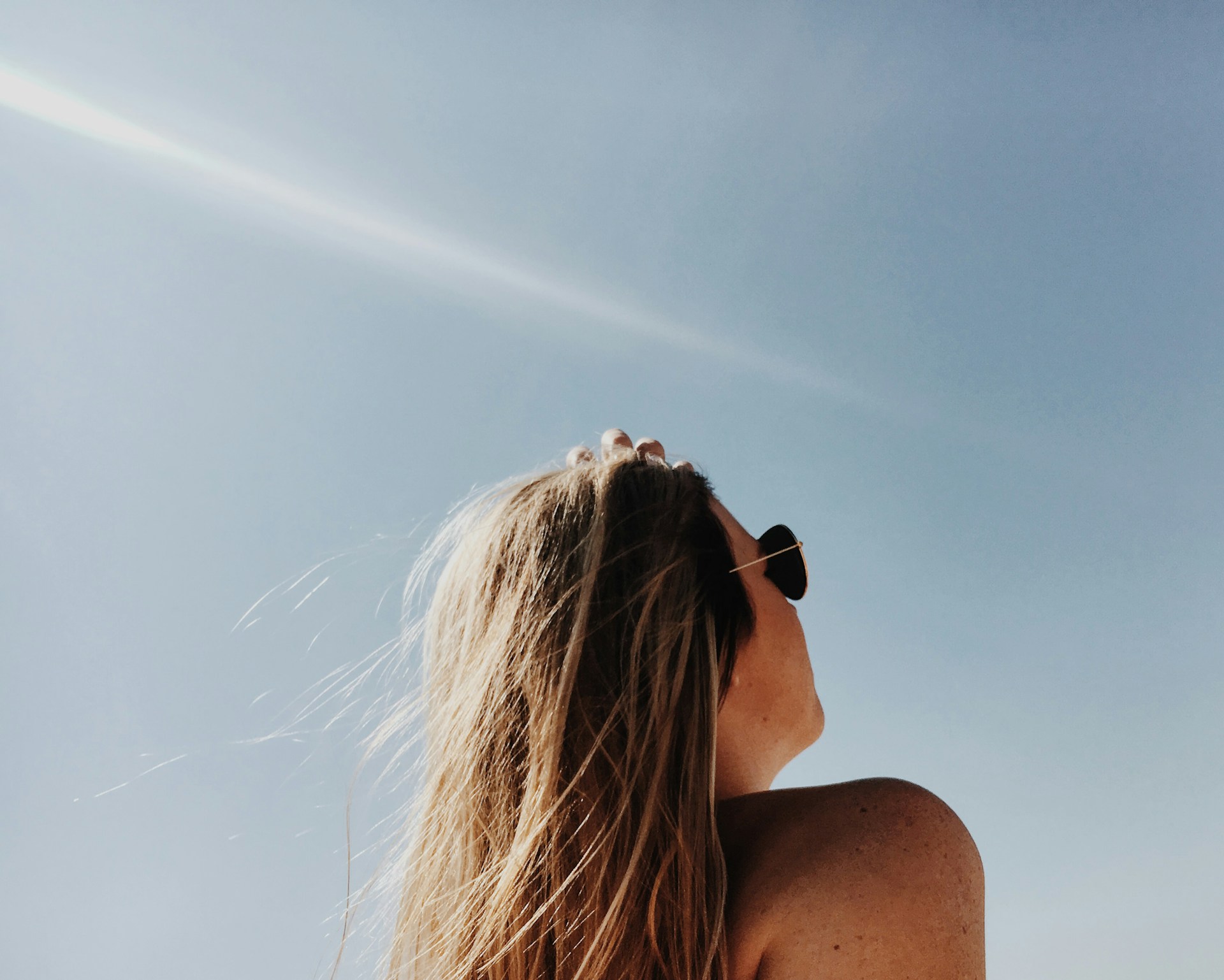 Woman with sunglasses looking up at a clear blue sky