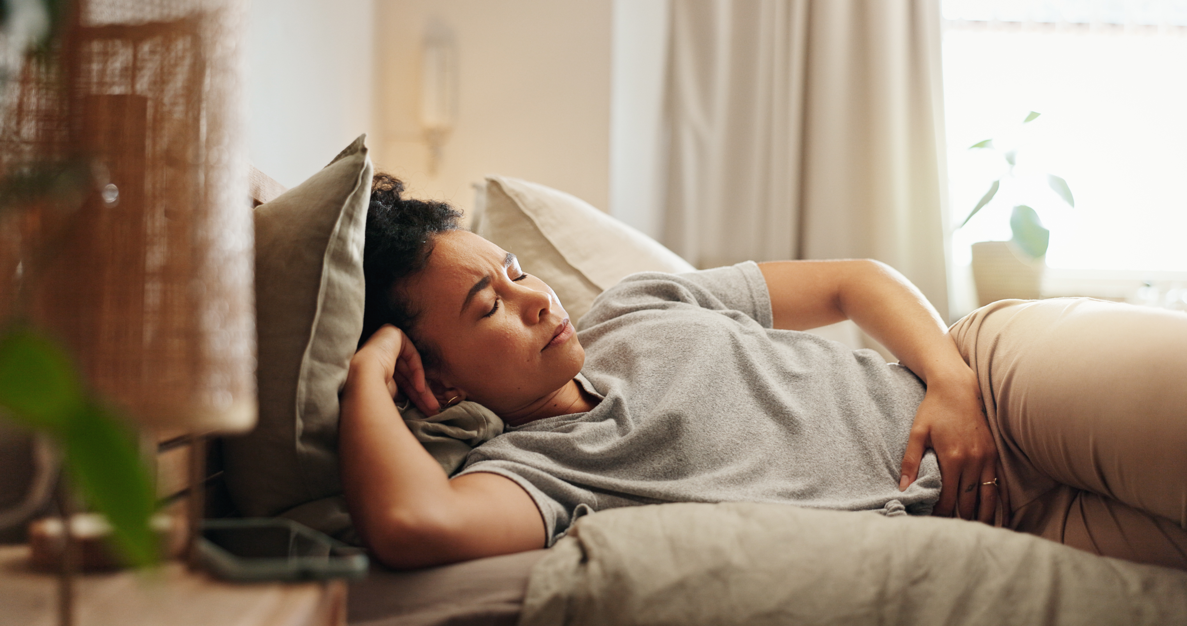 Woman lying on bed holding her stomach in discomfort