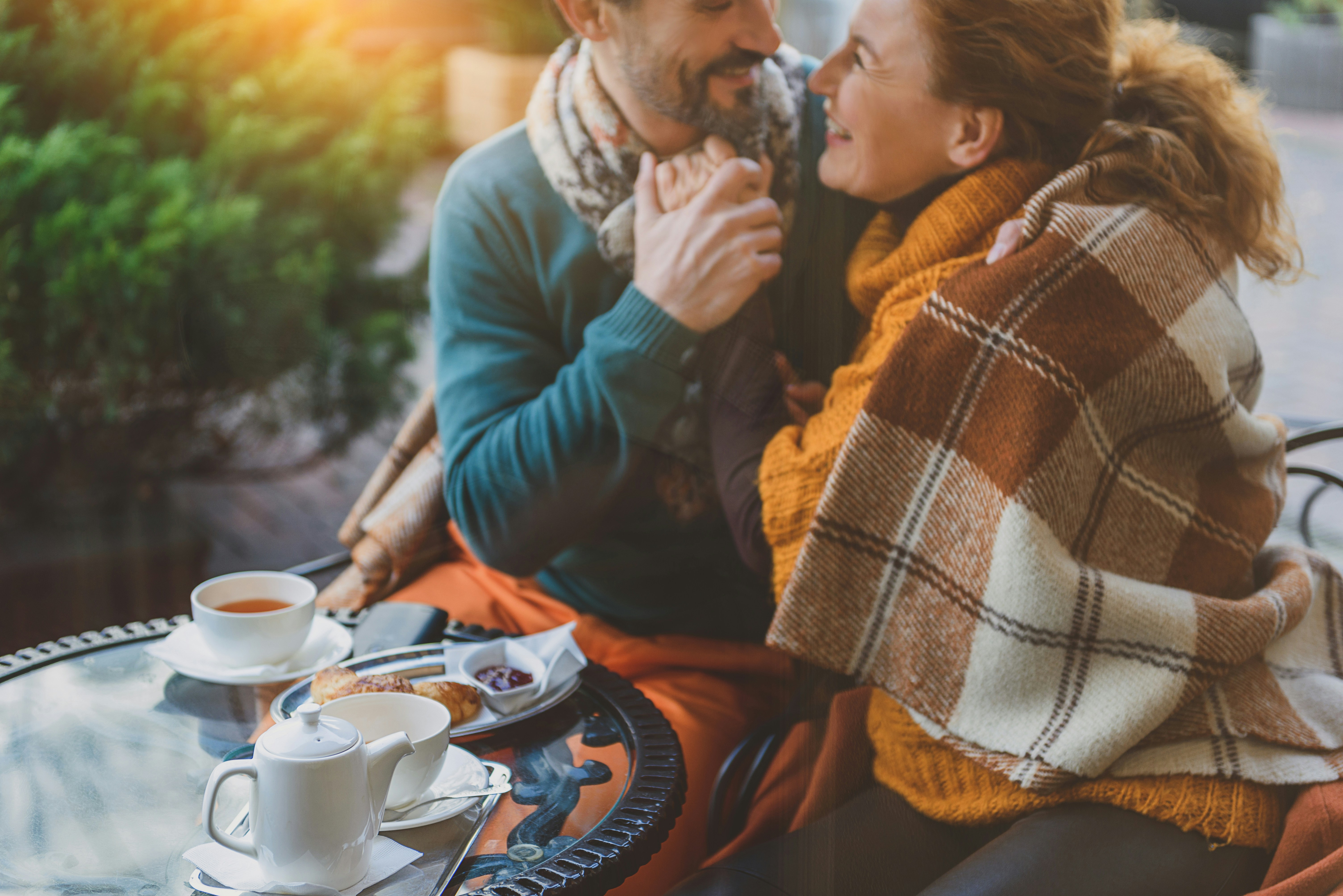 Couple cuddling and sitting outside with tea and pastries