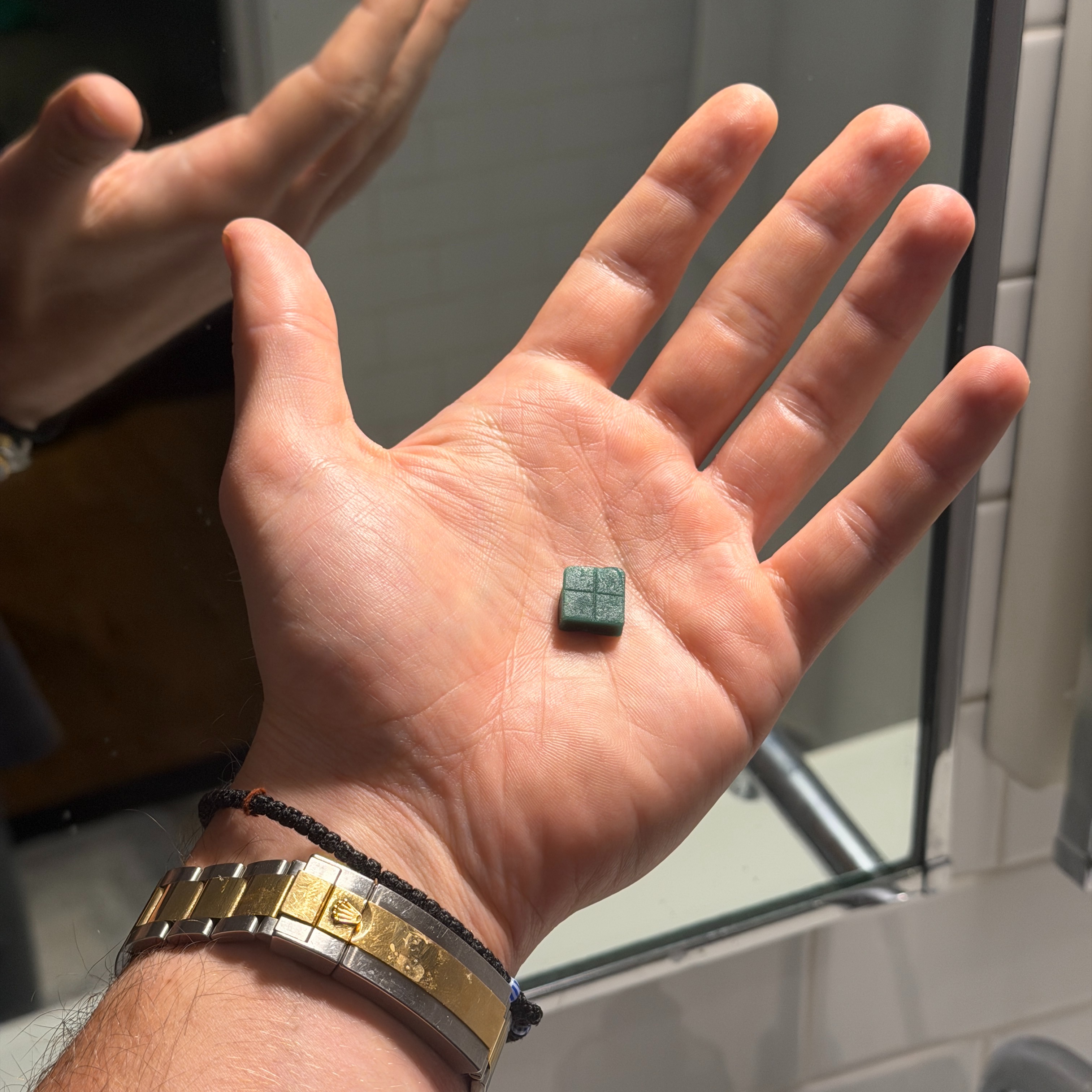 A green Rugiet Ready&reg; troche in the palm of a hand in a bathroom