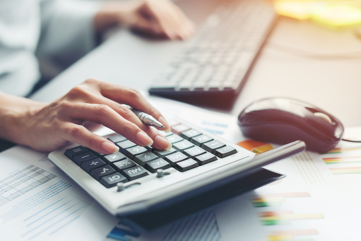 A hand making calculations on a calculator at a work desk