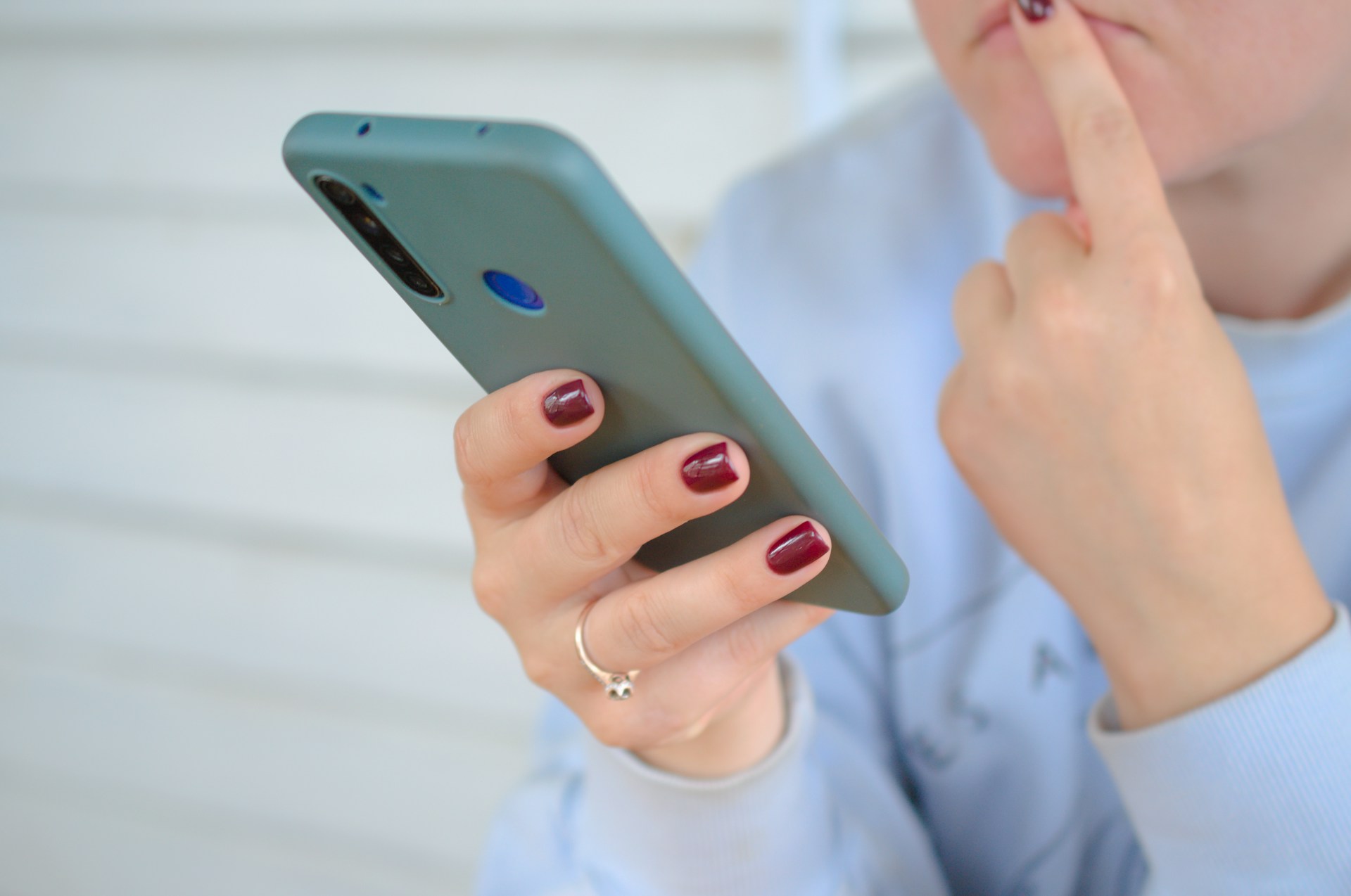 Close up of a woman looking at her phone with a finger pressed to her lips in thought