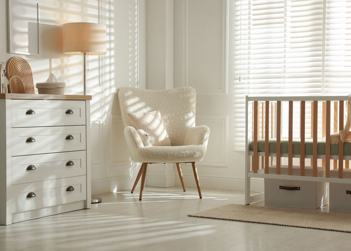 A white nursery room with a crib, dresser, and chair