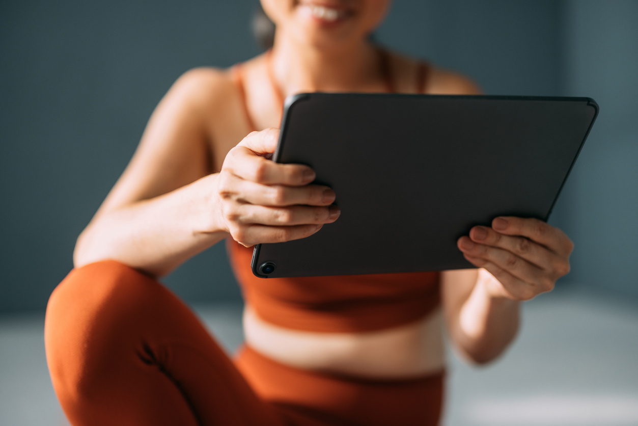 A woman in orange workout clothes smiling and holding a tablet