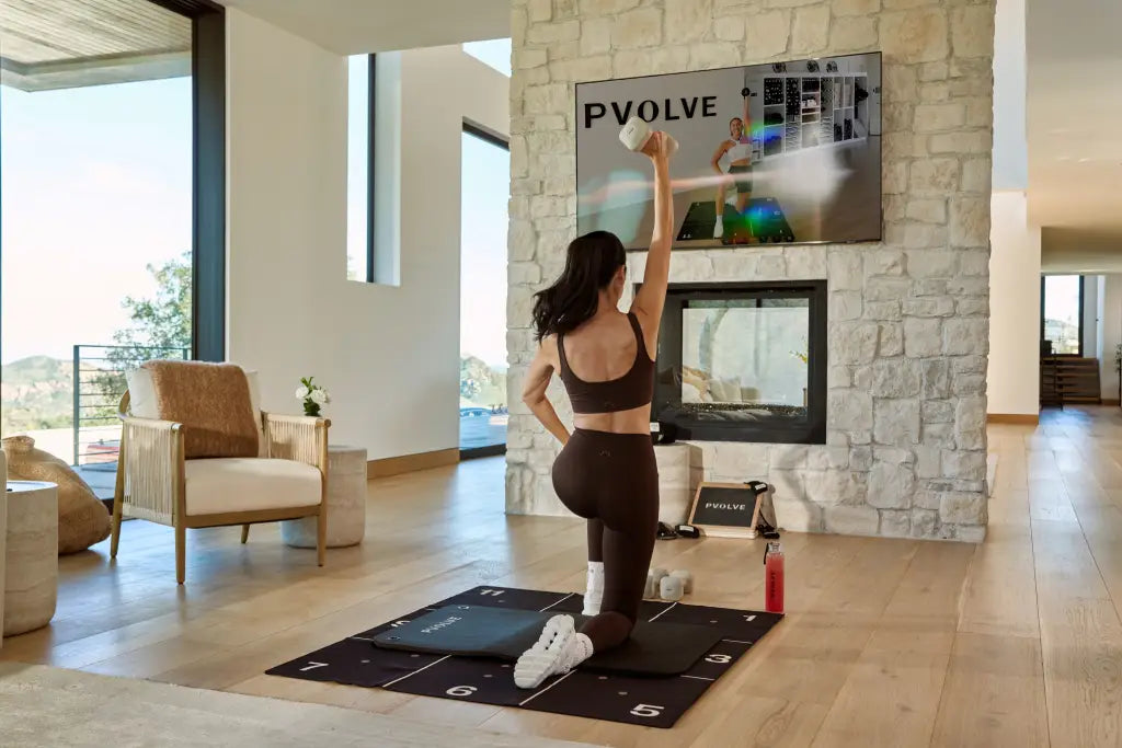 A woman following along with a PVOLVE workout in her living room