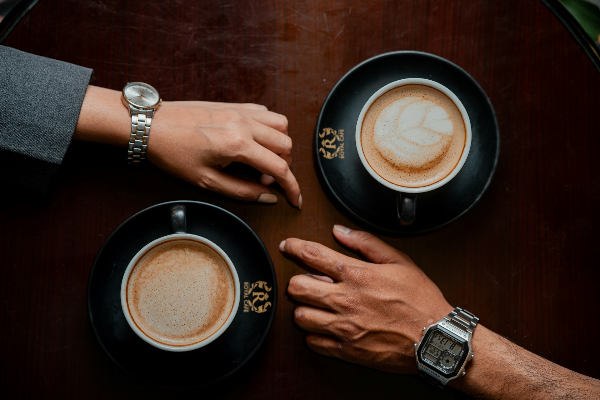 A woman and man's hand resting close to each other with lattes in mugs nearby