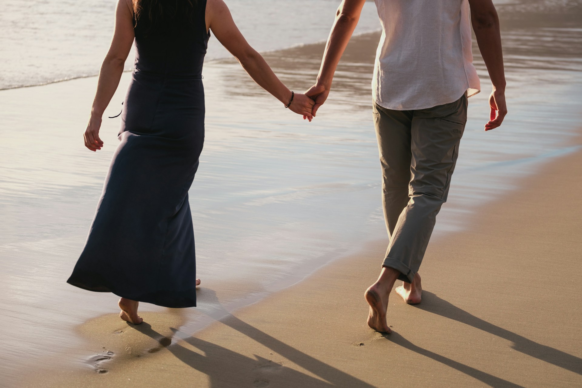 A man and woman holding hands as they walk on the beach