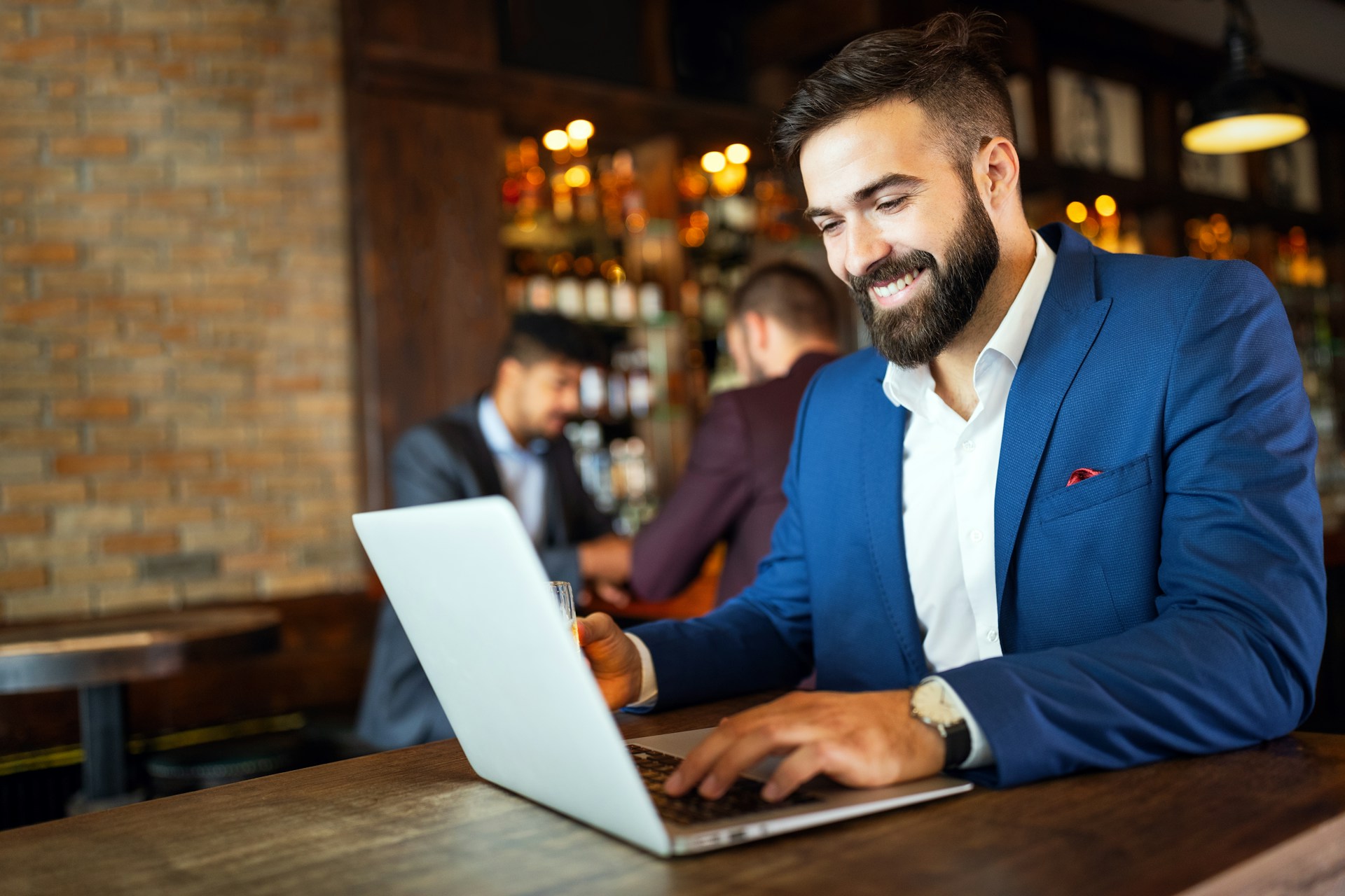 Man in a suit smiling at his laptop in a bar