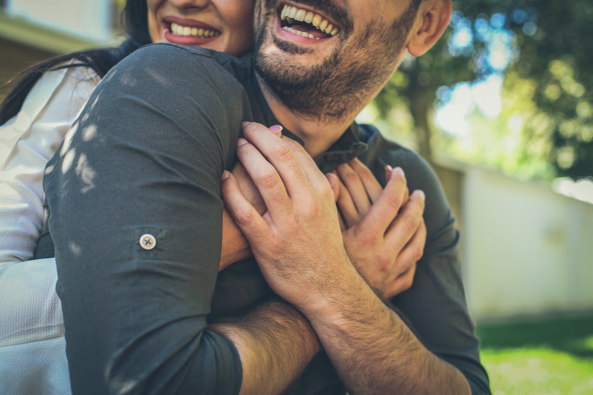 Couple smiling as the woman embraces the man from behind