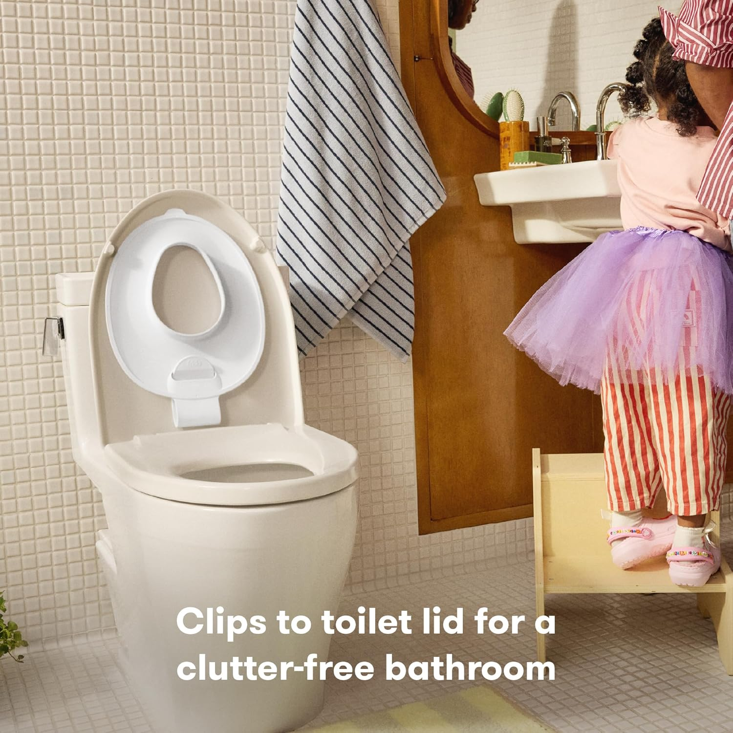 Little girl washes her hands in the sink beside the Frida Drop Down Potty Seat