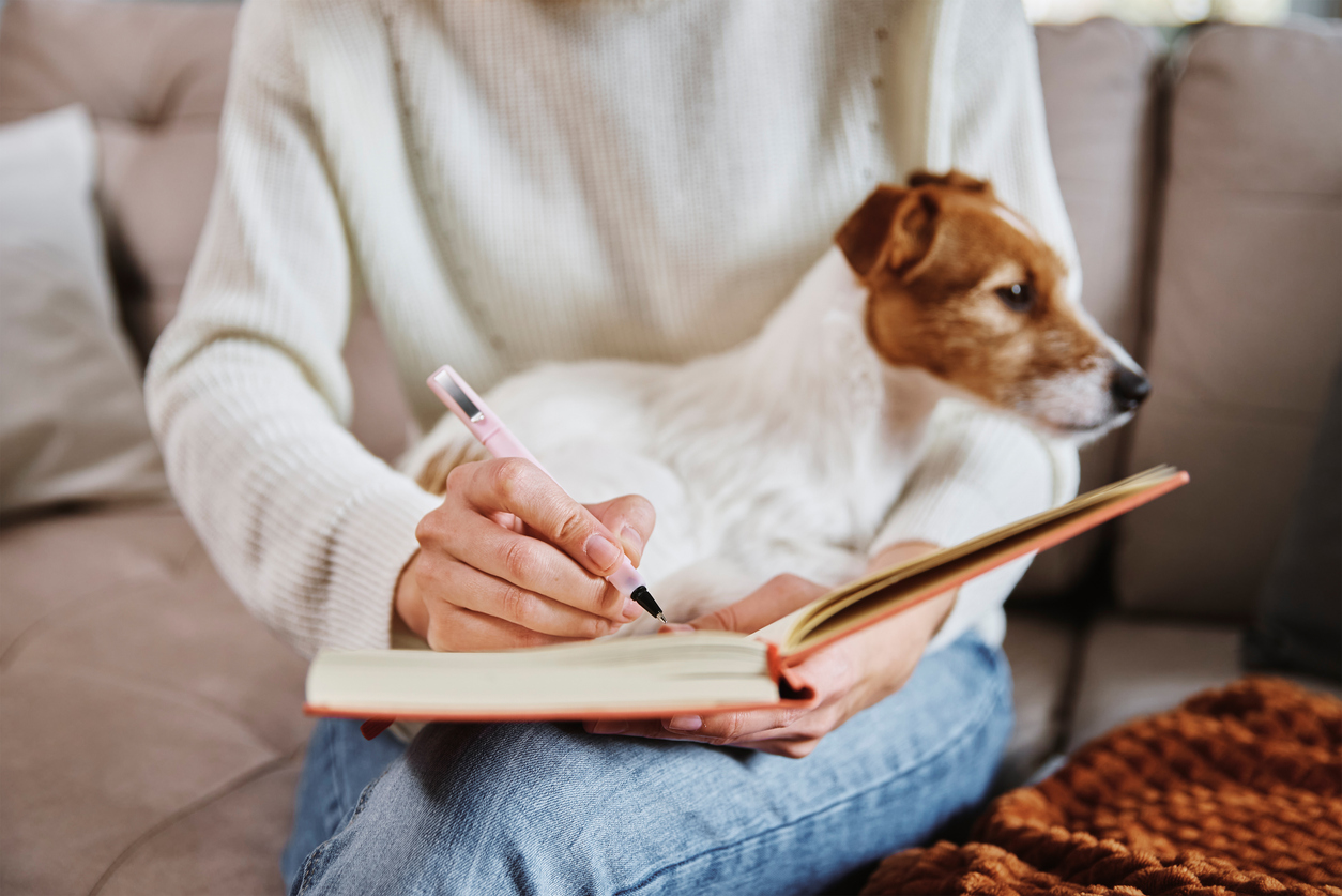 Woman holding her small dog and writing in a notebook