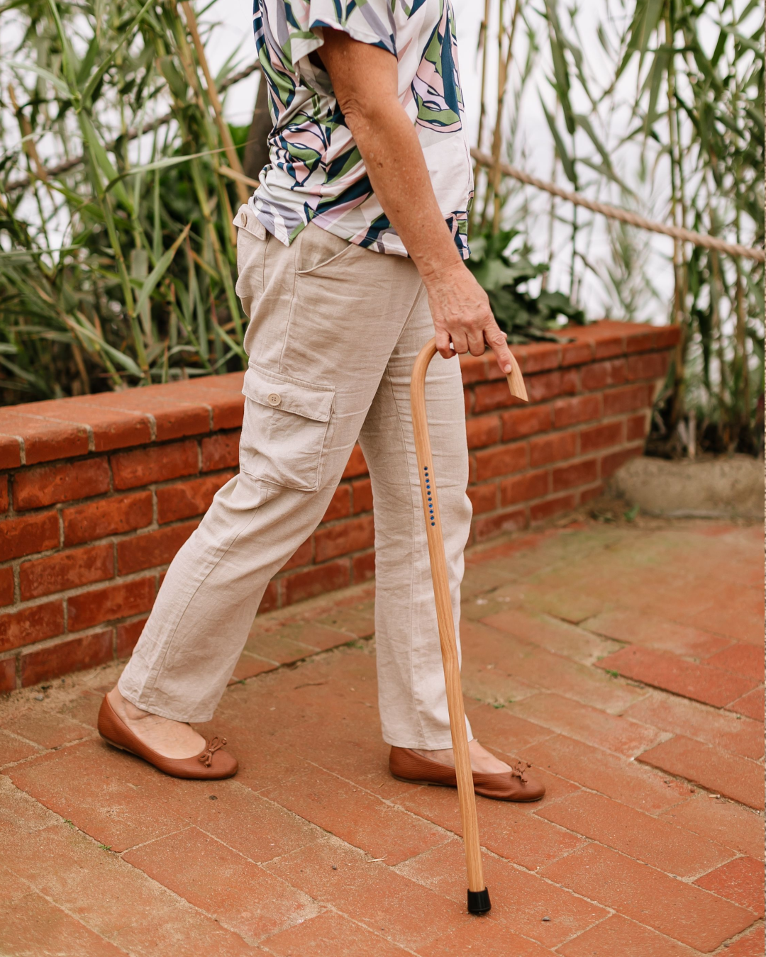 Woman confidently walking with a custom wooden cane on a brick path
