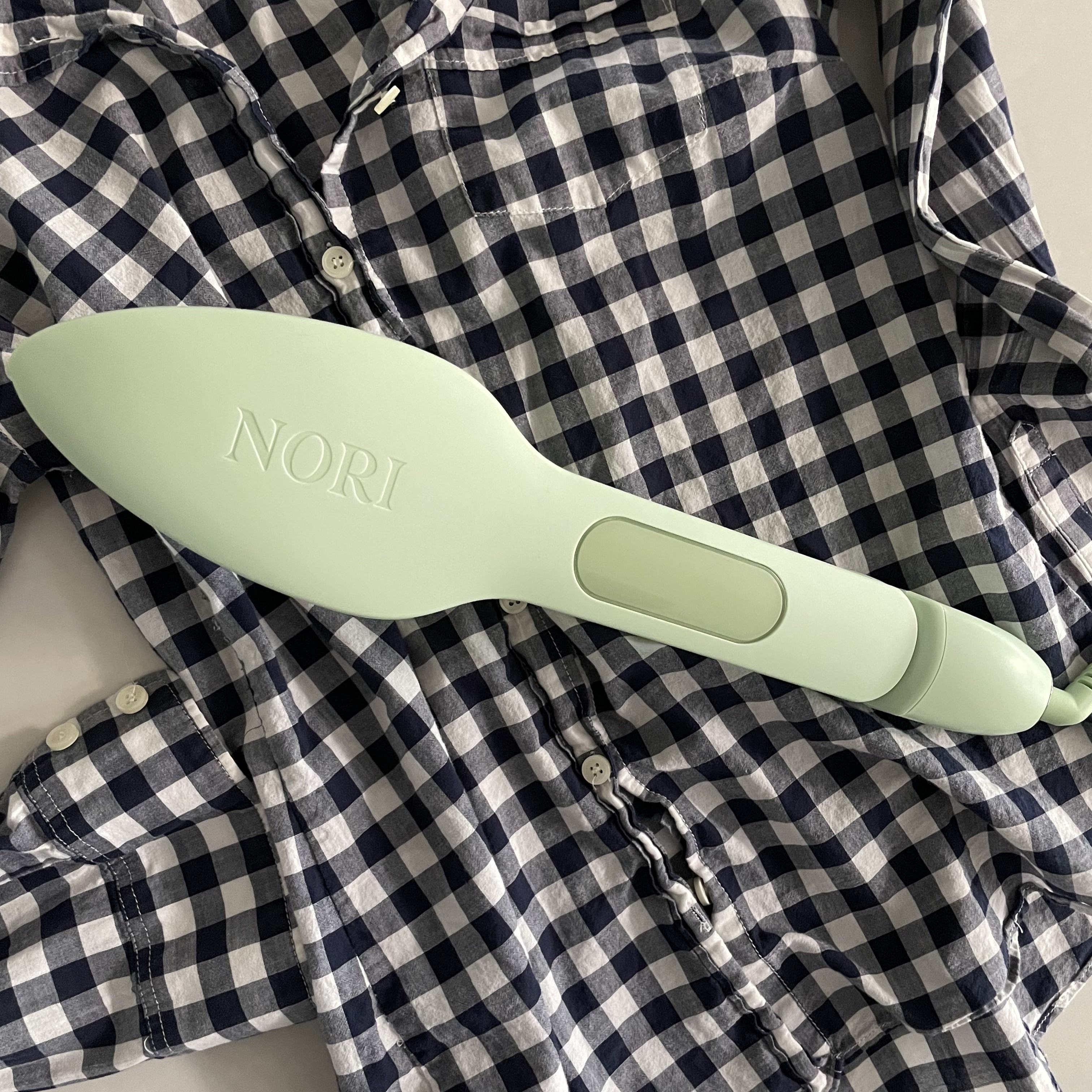 The Nori Press in green resting on a black and white checkered button up shirt