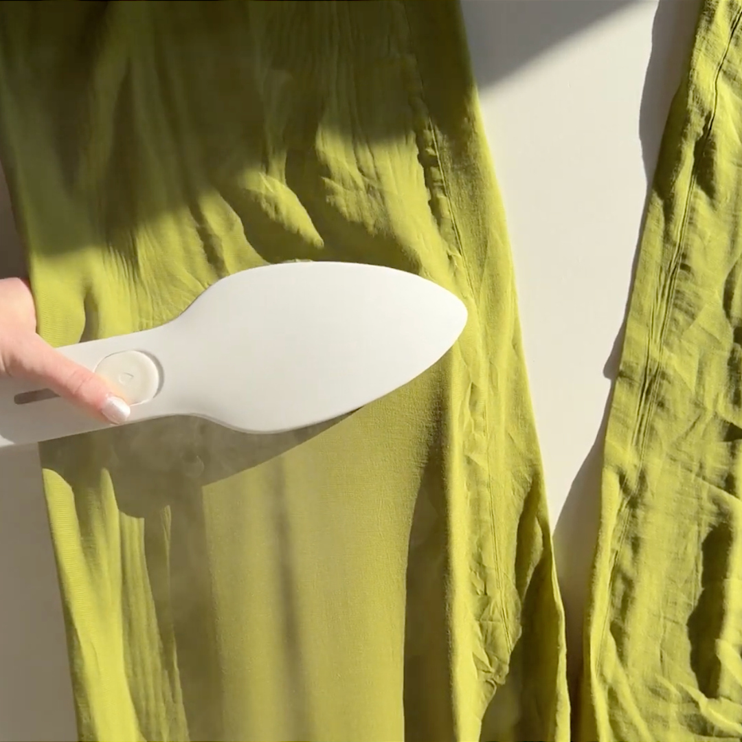 A hand uses a Nori Press steam iron on a lime green silk shirt to remove wrinkles.