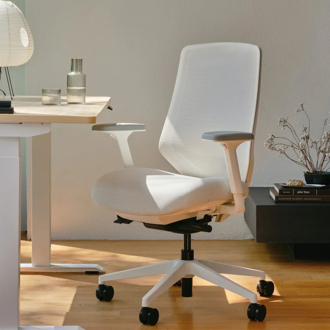 White Ergonomic Chair Pro in Shore Mesh next to a Woodgrain and White Duo Standing Desk in a warm, sunlit room