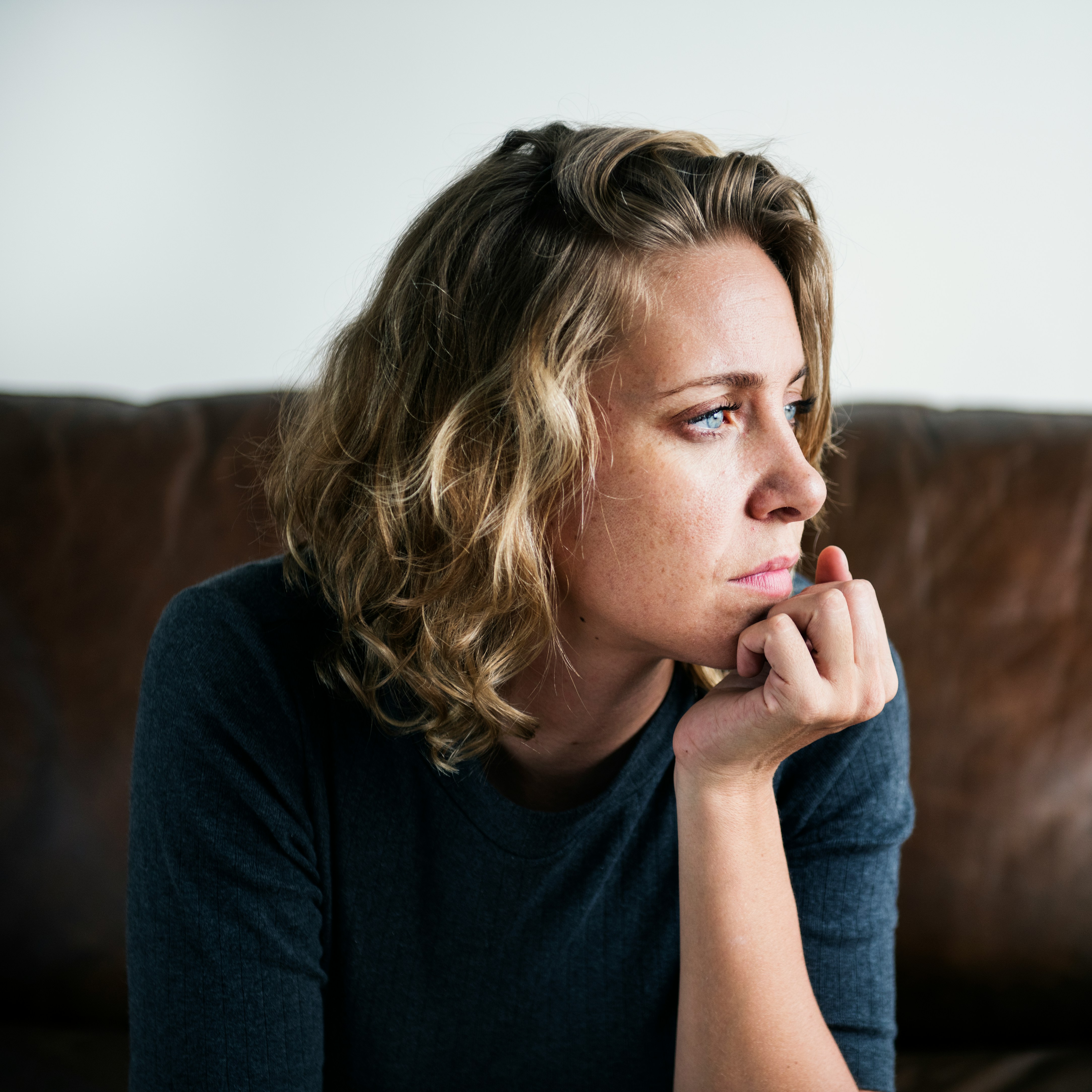 A woman sits on a couch, looking thoughtful and concerned