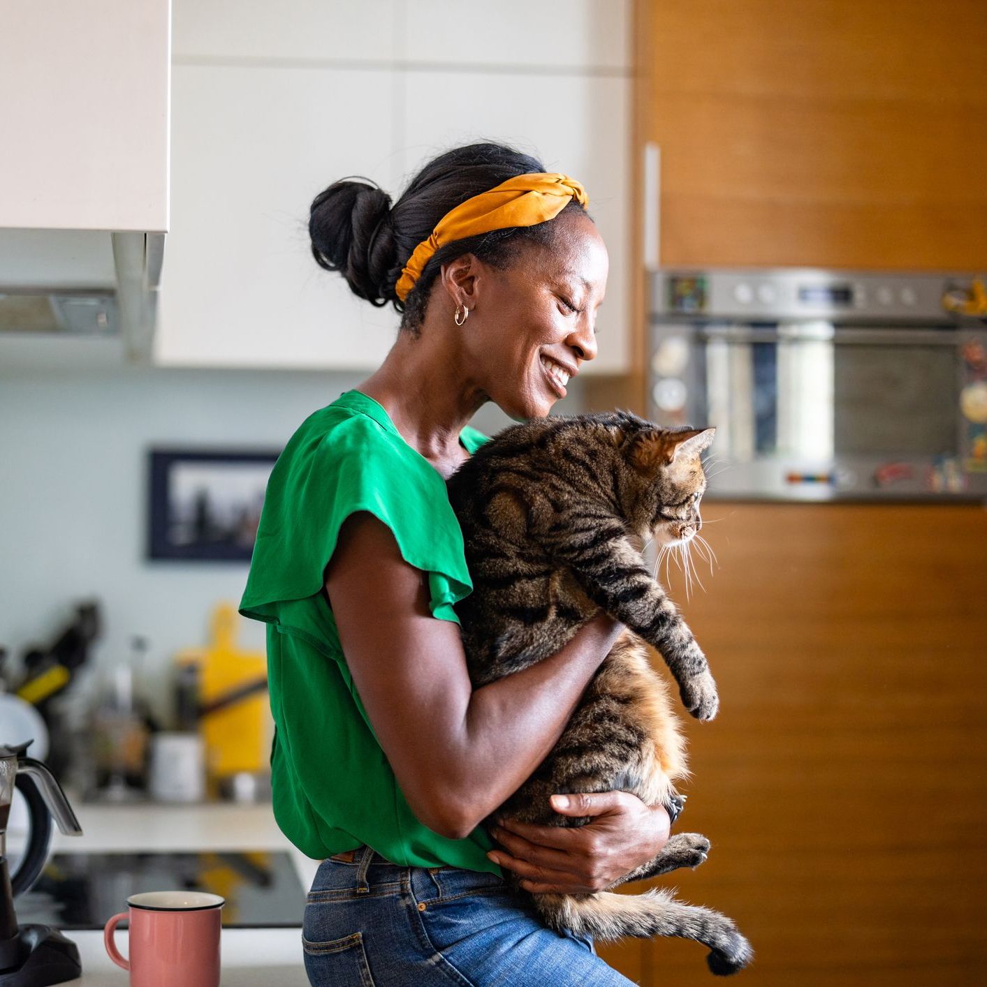 A woman smiles while holding a cat in her kitchen, reflecting a moment of joy