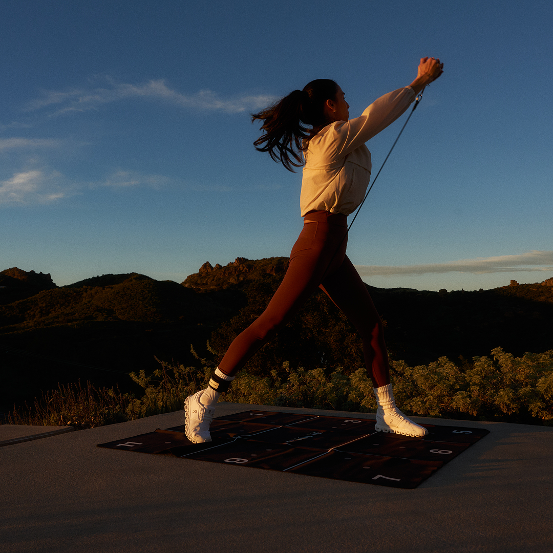 Outdoor Resistance Band Workout A woman exercises with resistance bands on a mat outdoors at sunset.