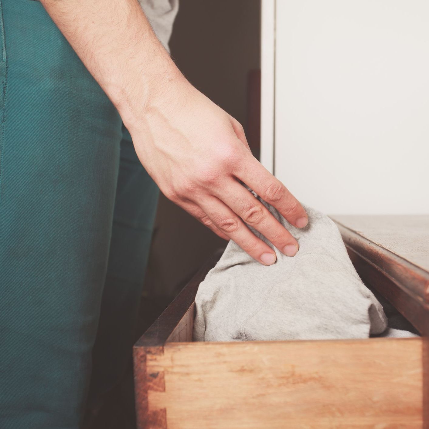 A person reaches into a drawer to pick up a pair of gray underwear