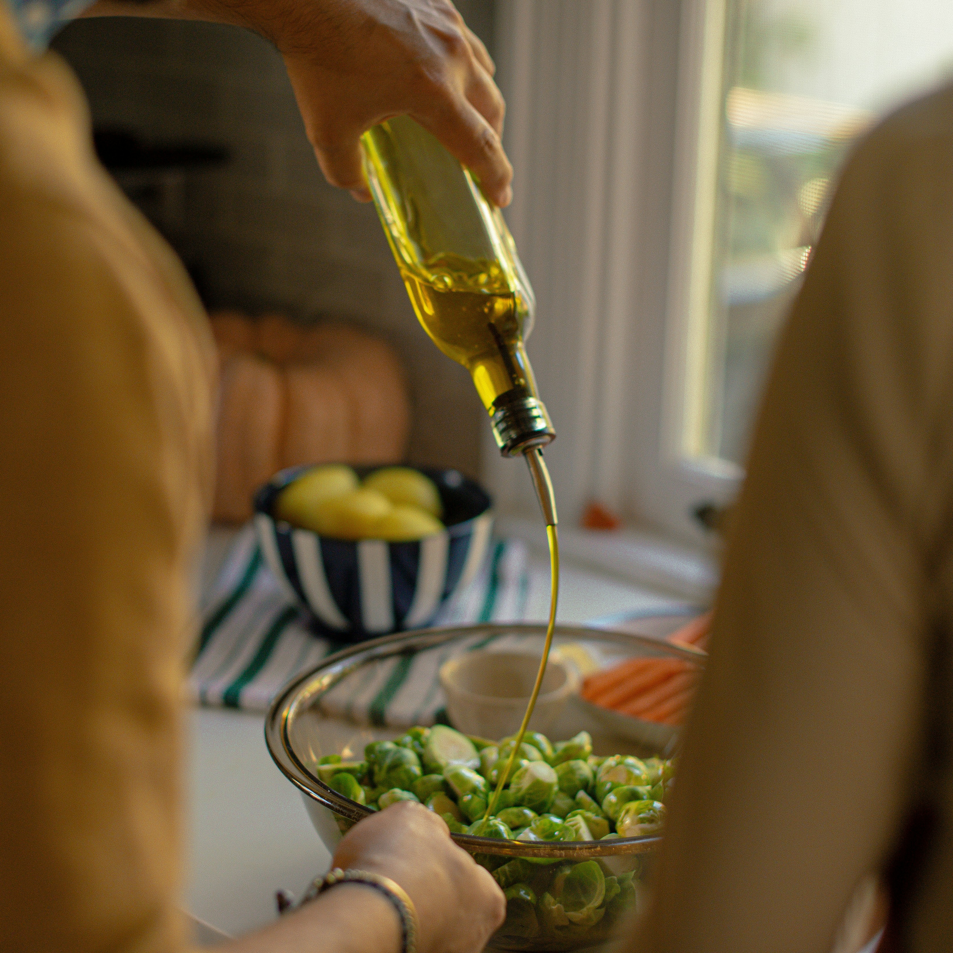 A person pours olive oil over Brussels sprouts in a kitchen setting