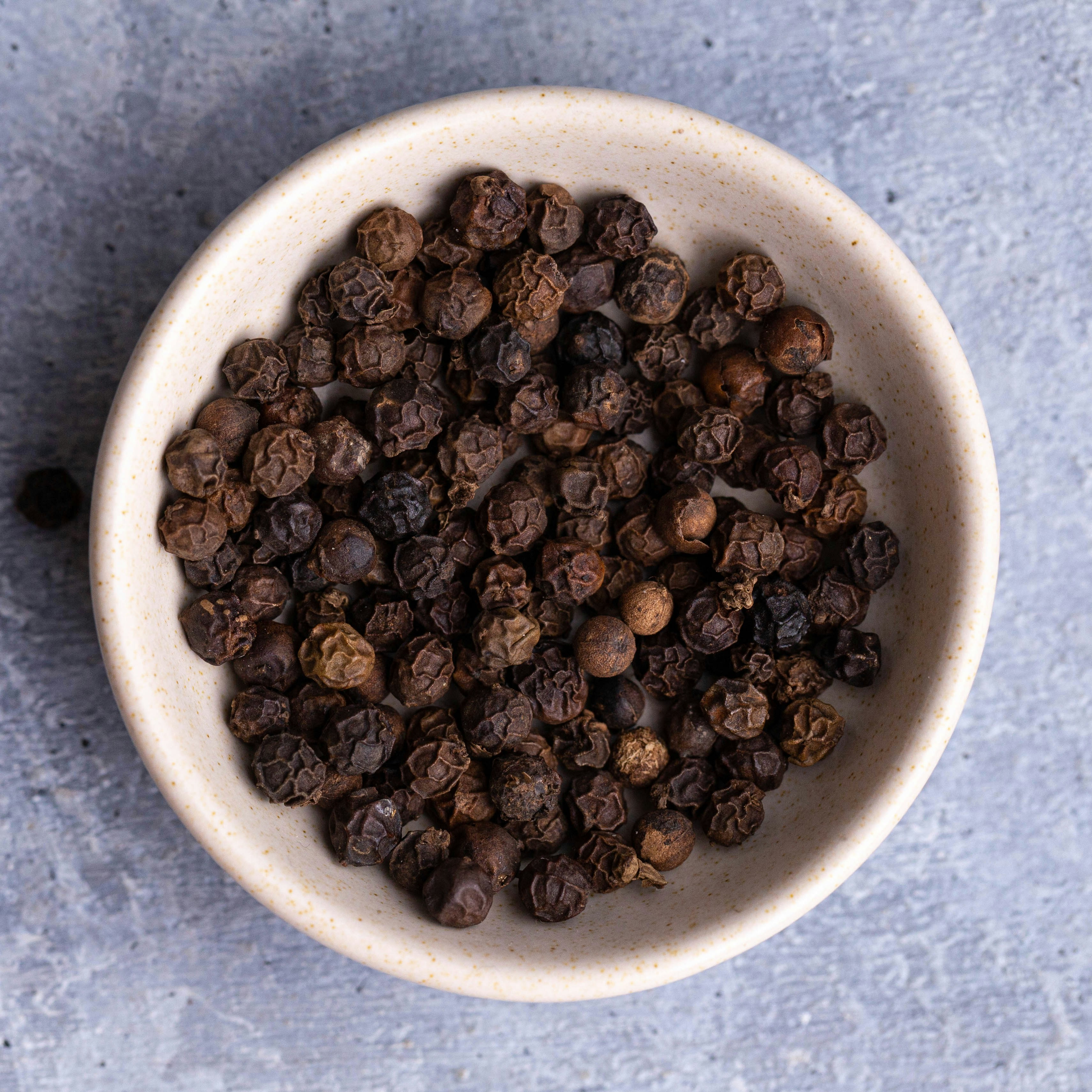 A bowl of whole black peppercorns, a key pantry staple for enhancing flavor