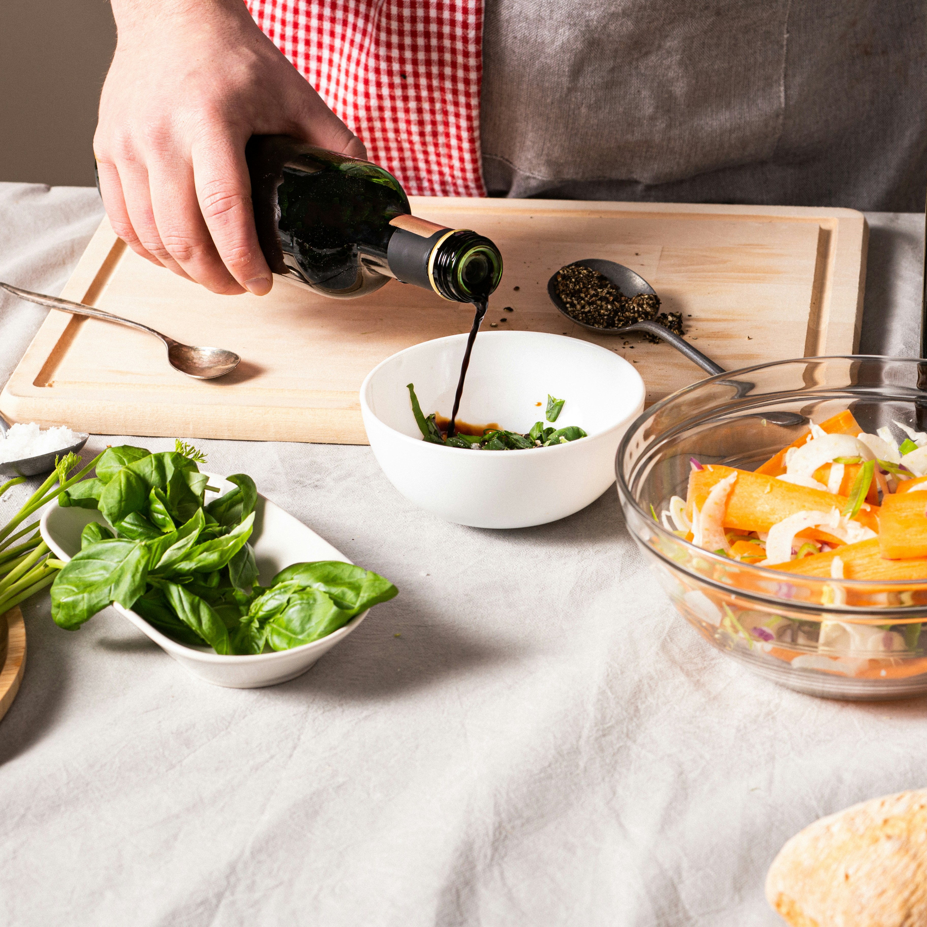Person pours balsamic vinegar into a bowl with fresh basil on a kitchen counter
