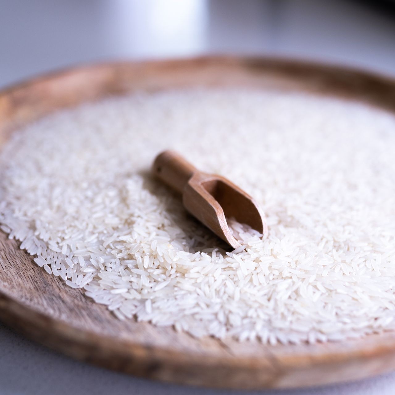 A wooden scoop rests on a plate of long-grain white rice, a pantry staple