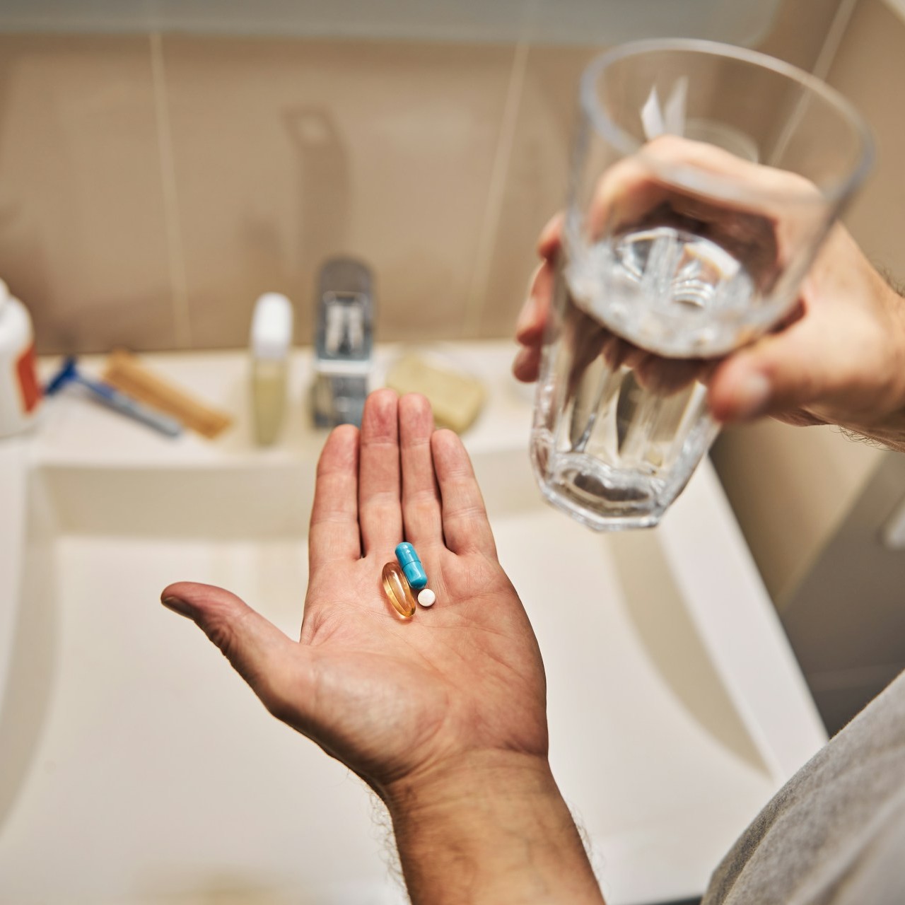 A person holds various pills and a glass of water