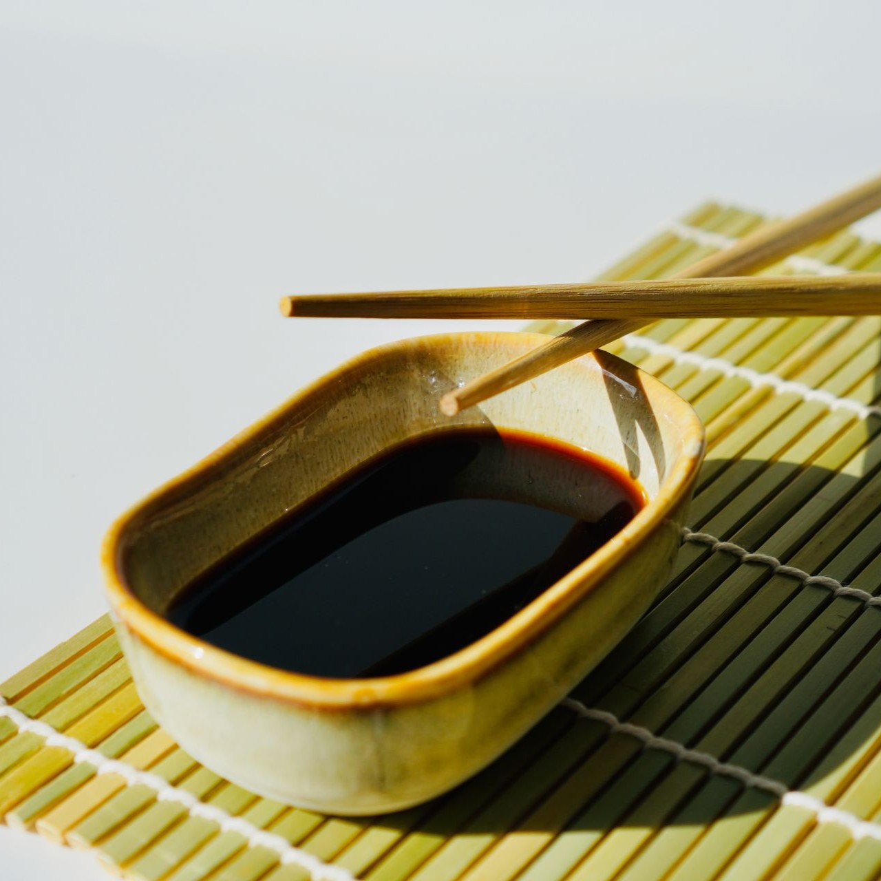 A small dish of soy sauce with chopsticks rests on a bamboo mat.