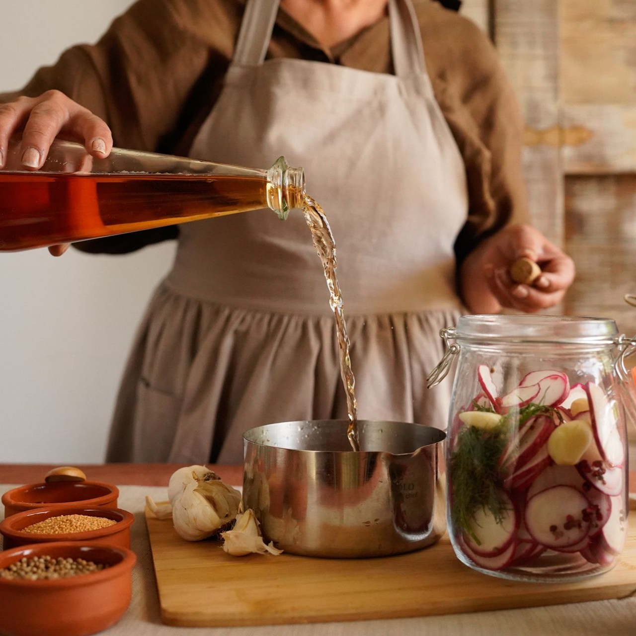 Person pours vinegar into a pot next to a jar of pickling vegetables