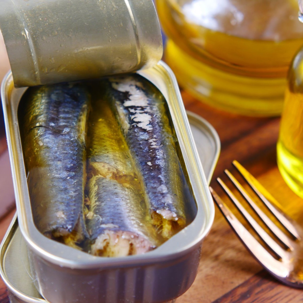 Open Tin of Sardines An open tin of sardines in oil sits on a wooden surface with a fork nearby