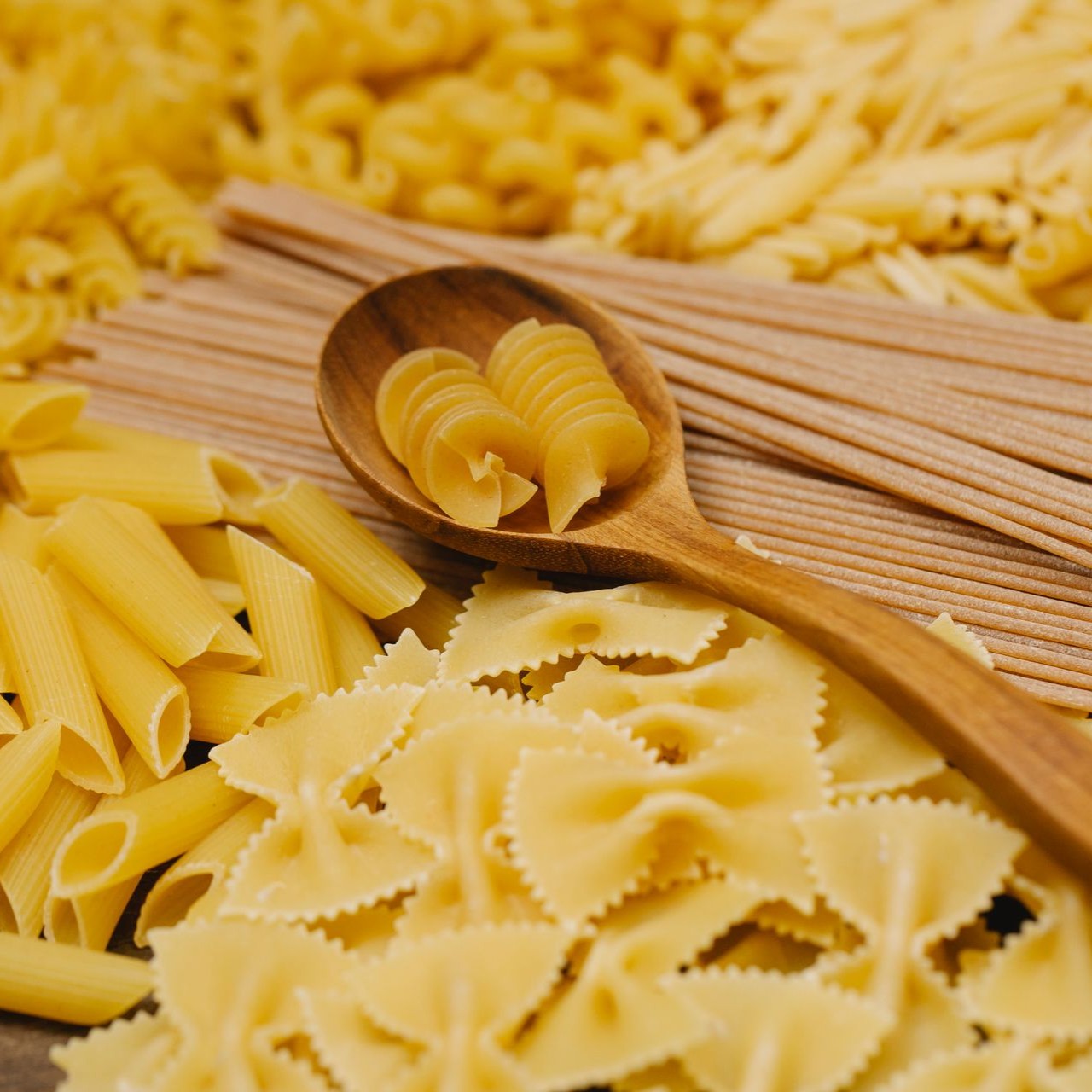 Assorted Dry Pasta Various types of dry pasta, including fusilli and penne, are displayed with a wooden spoon