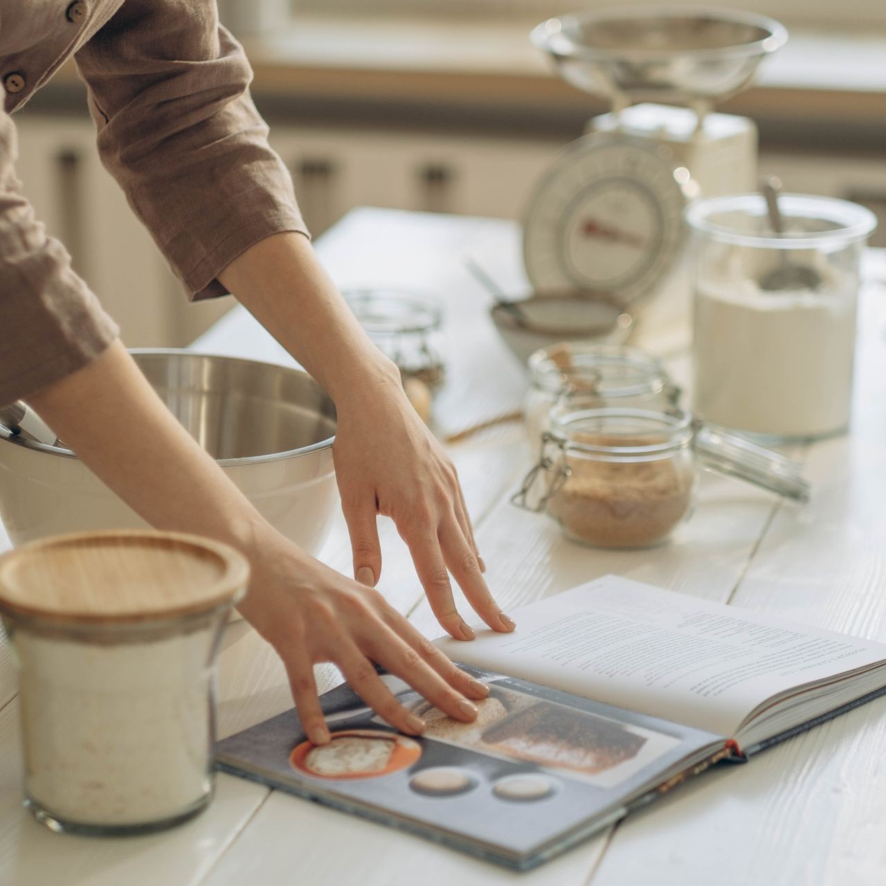 Person Reading Cookbook Person preparing ingredients with an open cookbook in a kitchen