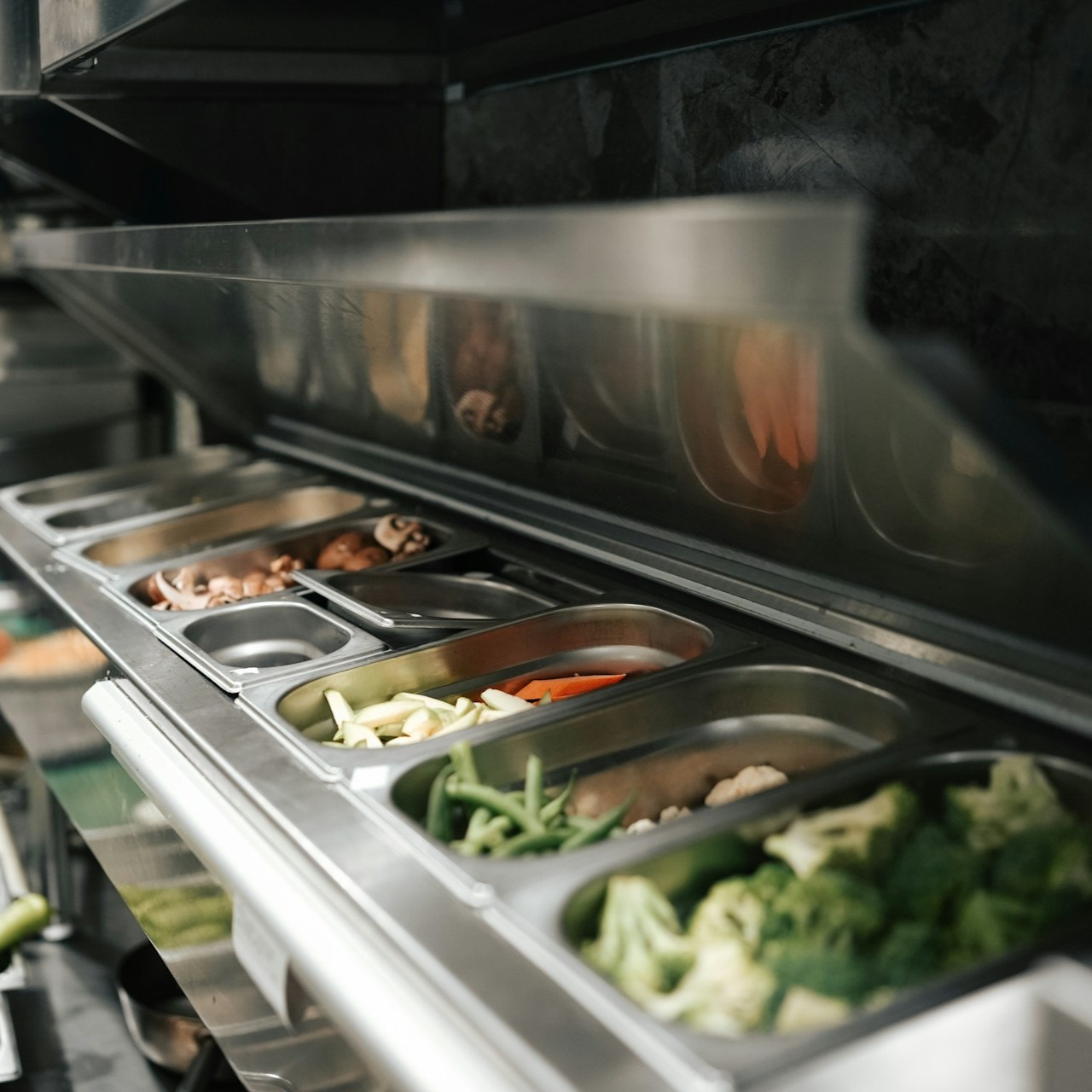 Mise en Place with Fresh Vegetables Stainless steel containers hold various fresh vegetables in a kitchen