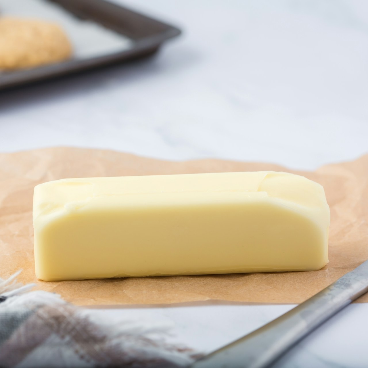 Stick of Butter on Parchment A stick of butter rests on parchment paper with a knife nearby
