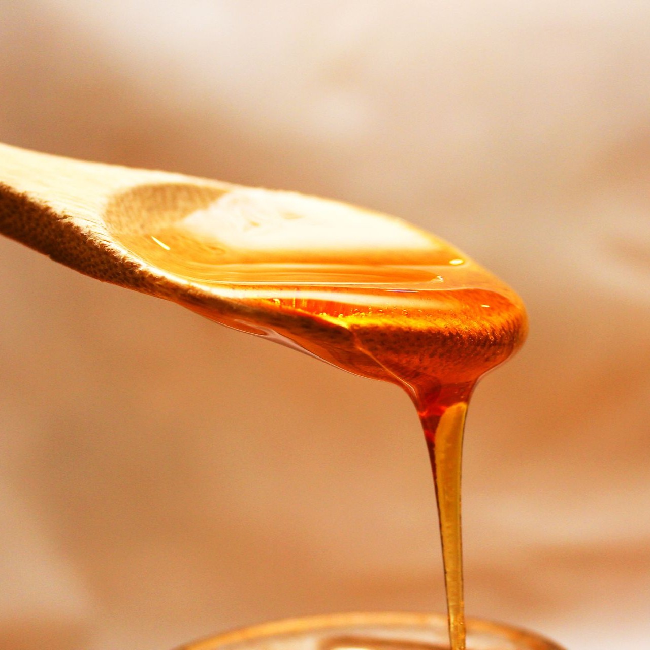 Honey Dripping from Spoon Honey drips from a wooden spoon into a jar below