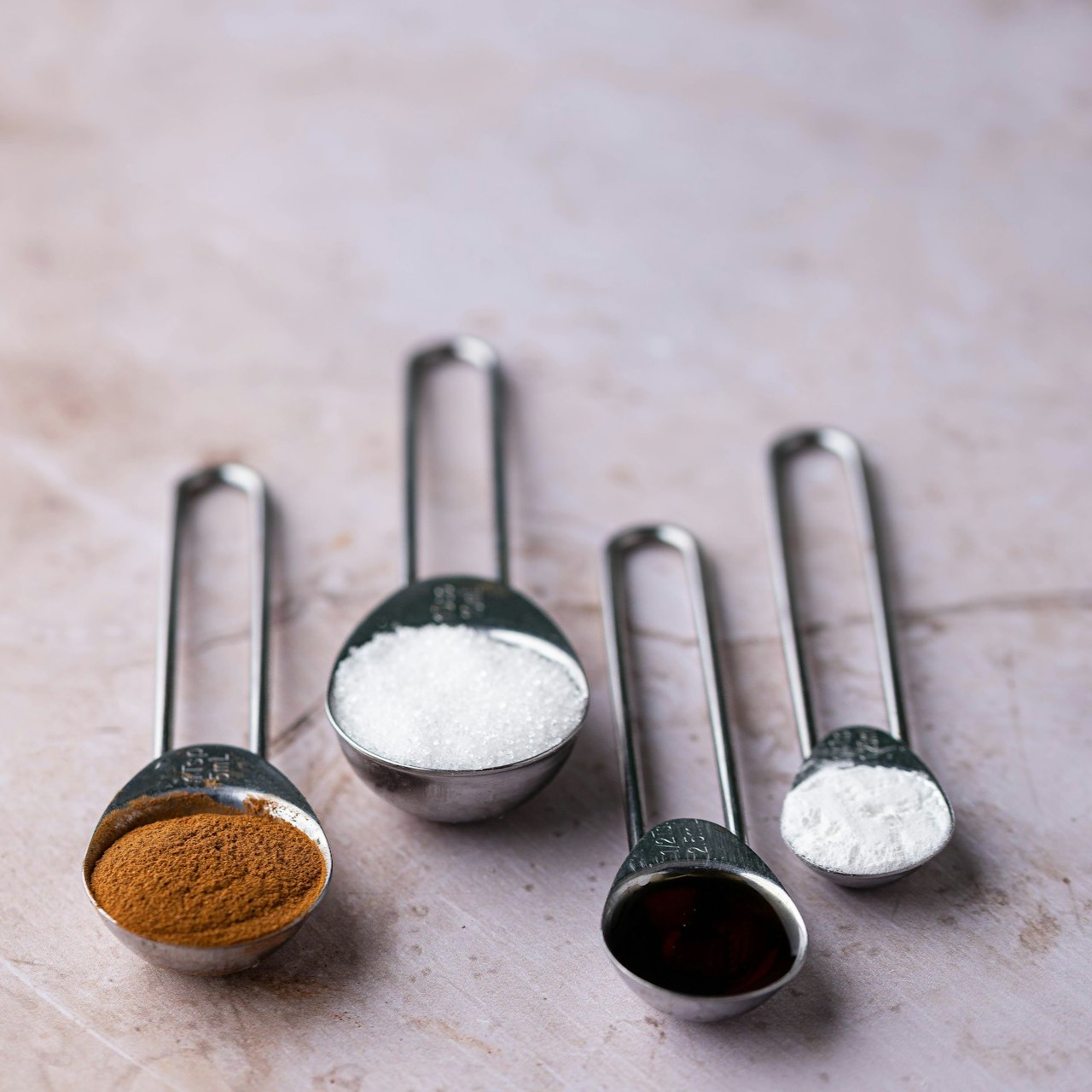 Baking Ingredients in Measuring Spoons Four measuring spoons with baking ingredients on a marble surface