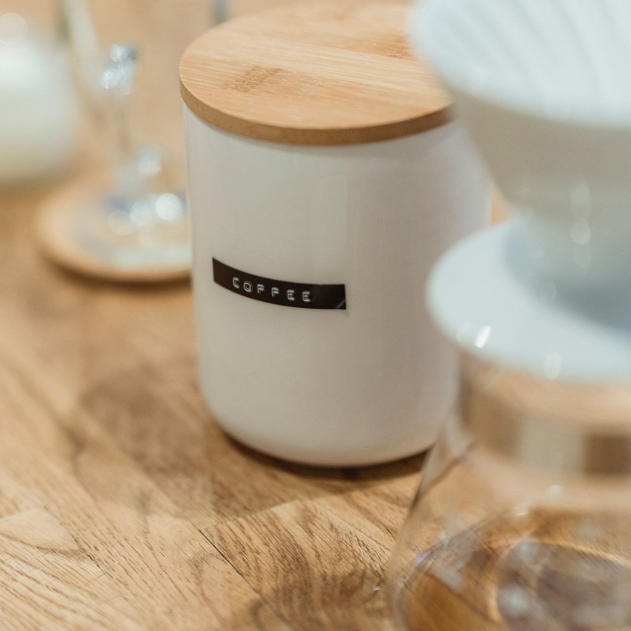 White Coffee Container on Table A white coffee container with a wooden lid sits on a wooden table