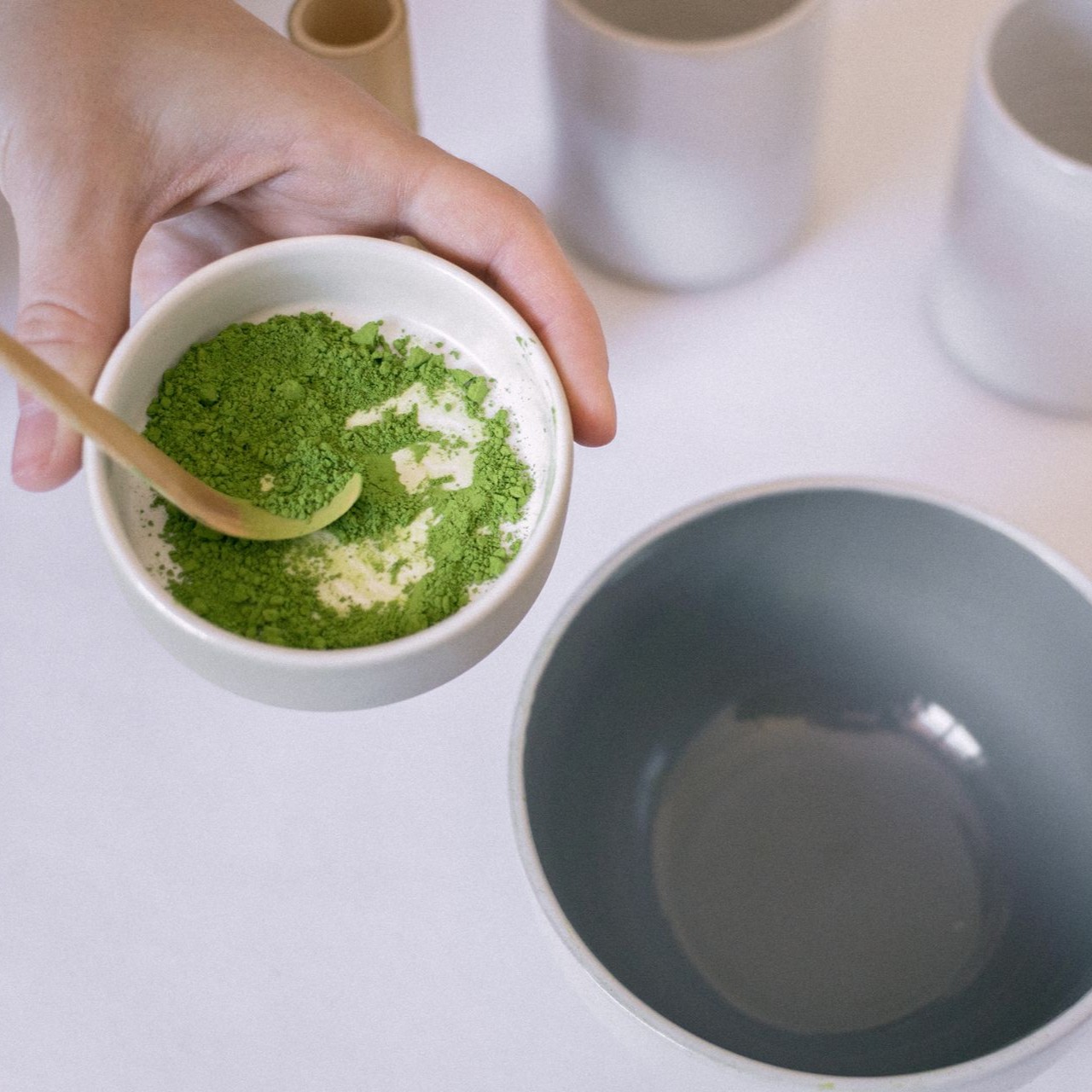 Preparing Matcha Tea Person holds a bowl of green matcha powder with a wooden spoon
